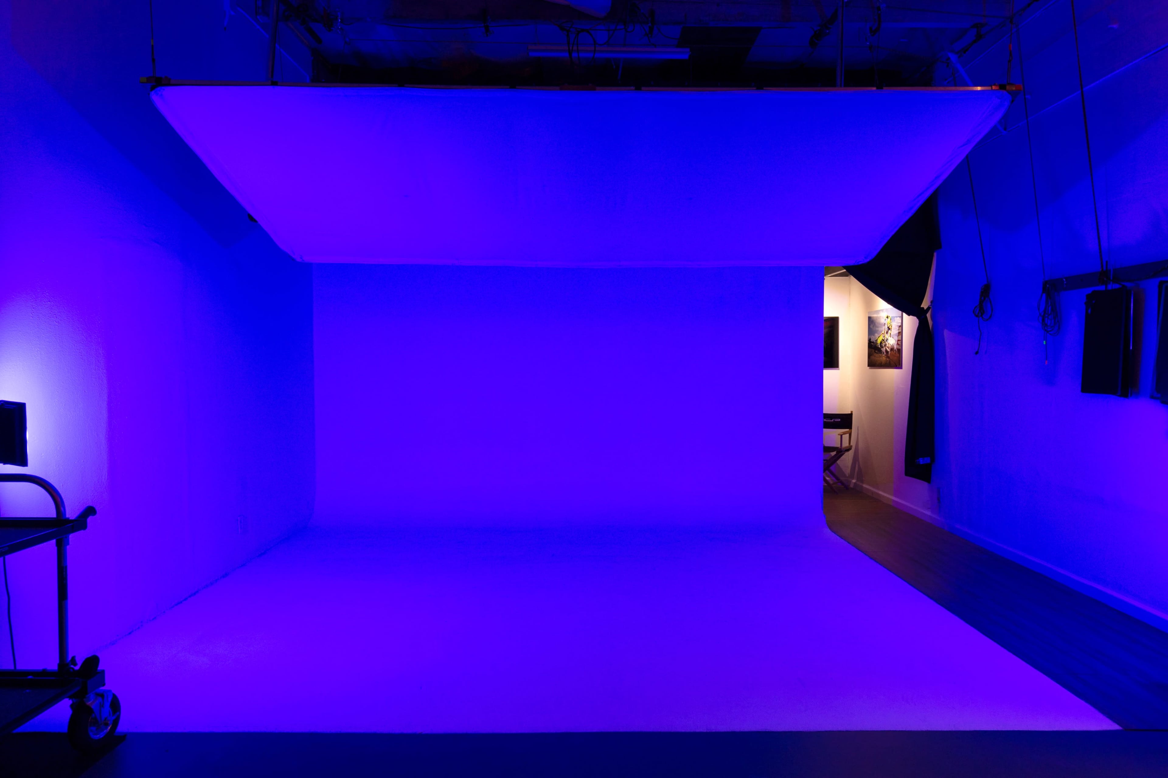 A photo studio with a large blue backdrop and a doorway leading to another room.