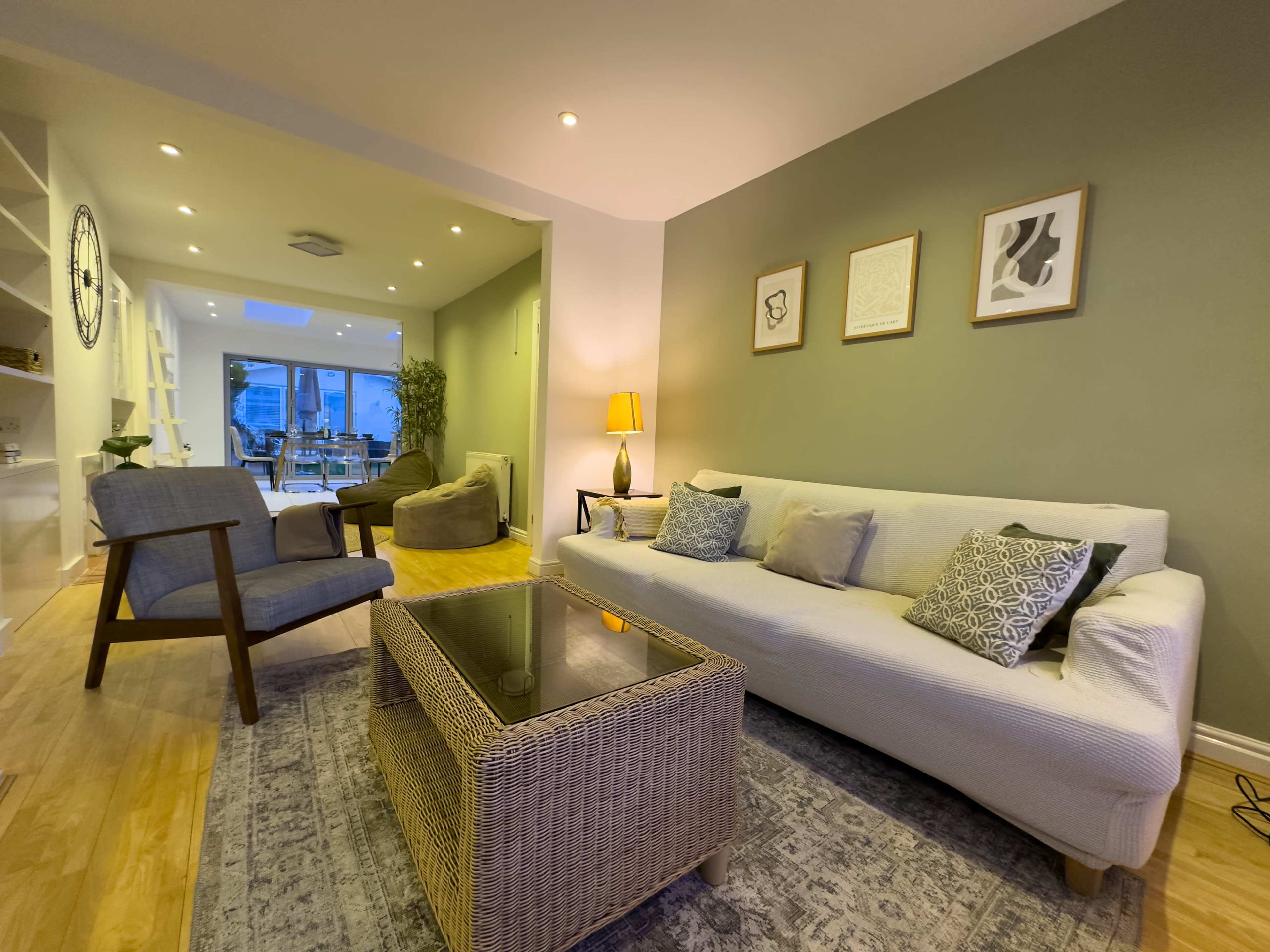 A modern living room with a white sofa, a glass-top coffee table, and a small reading chair, illuminated by soft lighting.