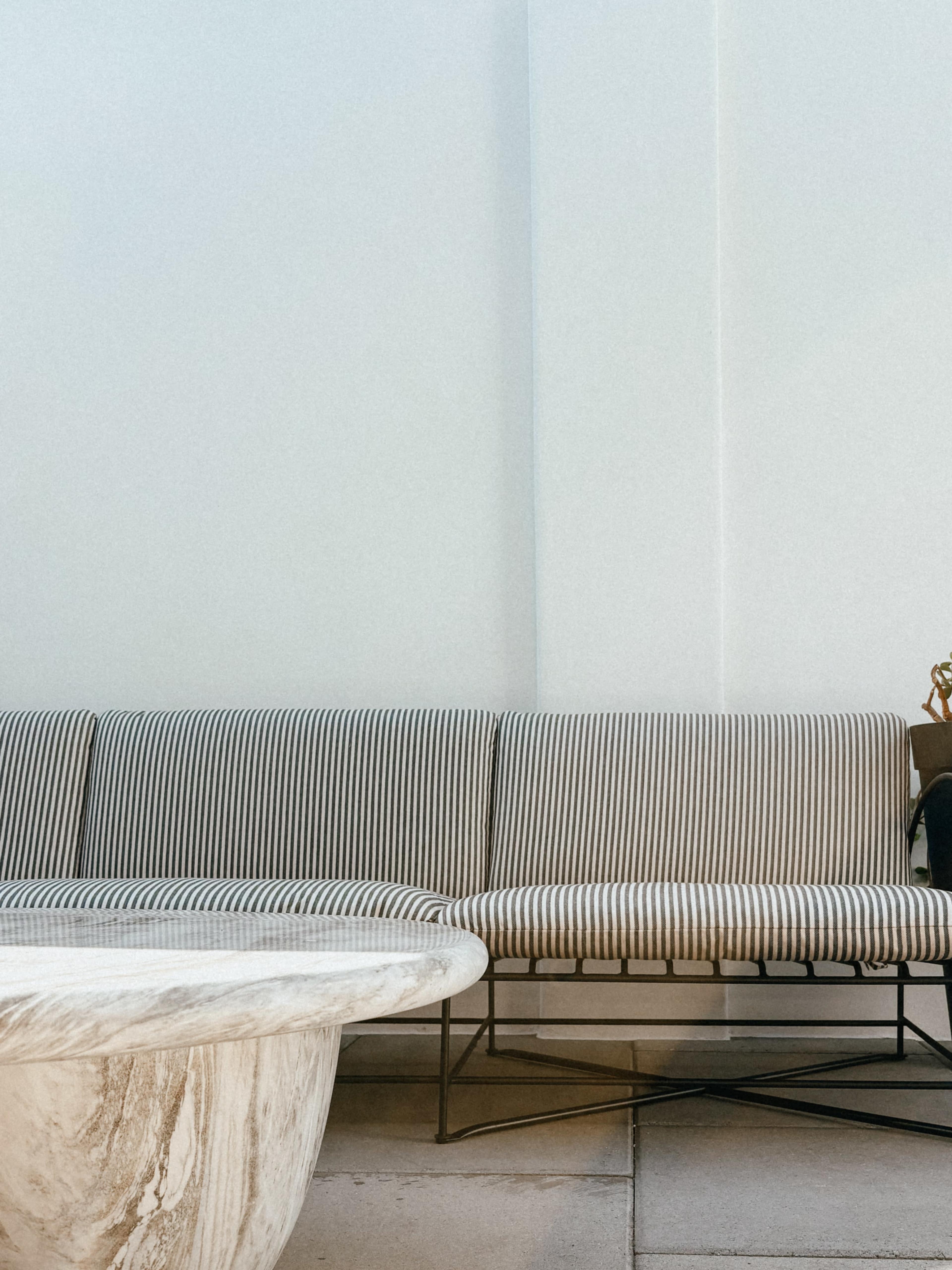 The image shows a striped sofa adjacent to a round marble coffee table, set against a minimalistic light-colored wall.