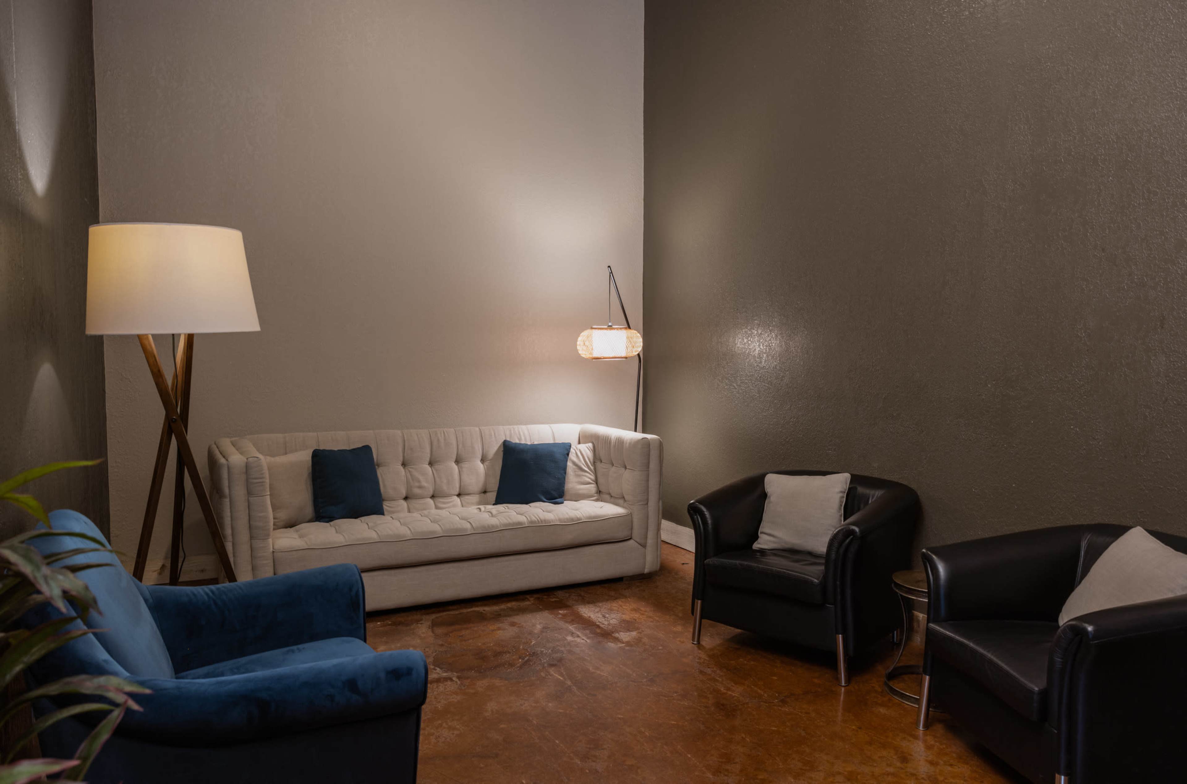 A cozy sitting area features a light-colored couch with blue accents, two black armchairs, a standing lamp, and a wall-mounted light.