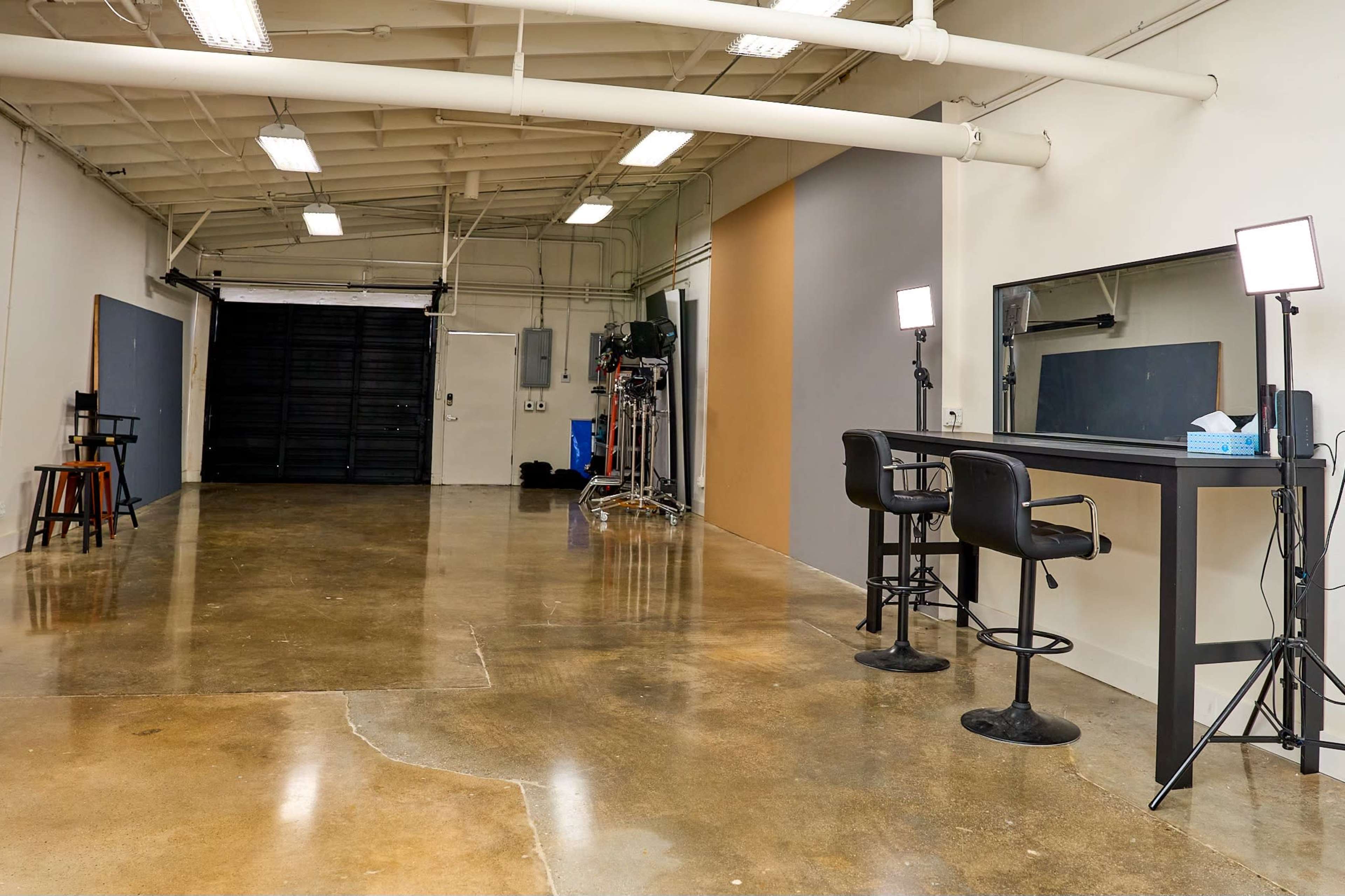A spacious, well-lit studio with a polished concrete floor, two black chairs, a large mirror, and a backdrop area.
