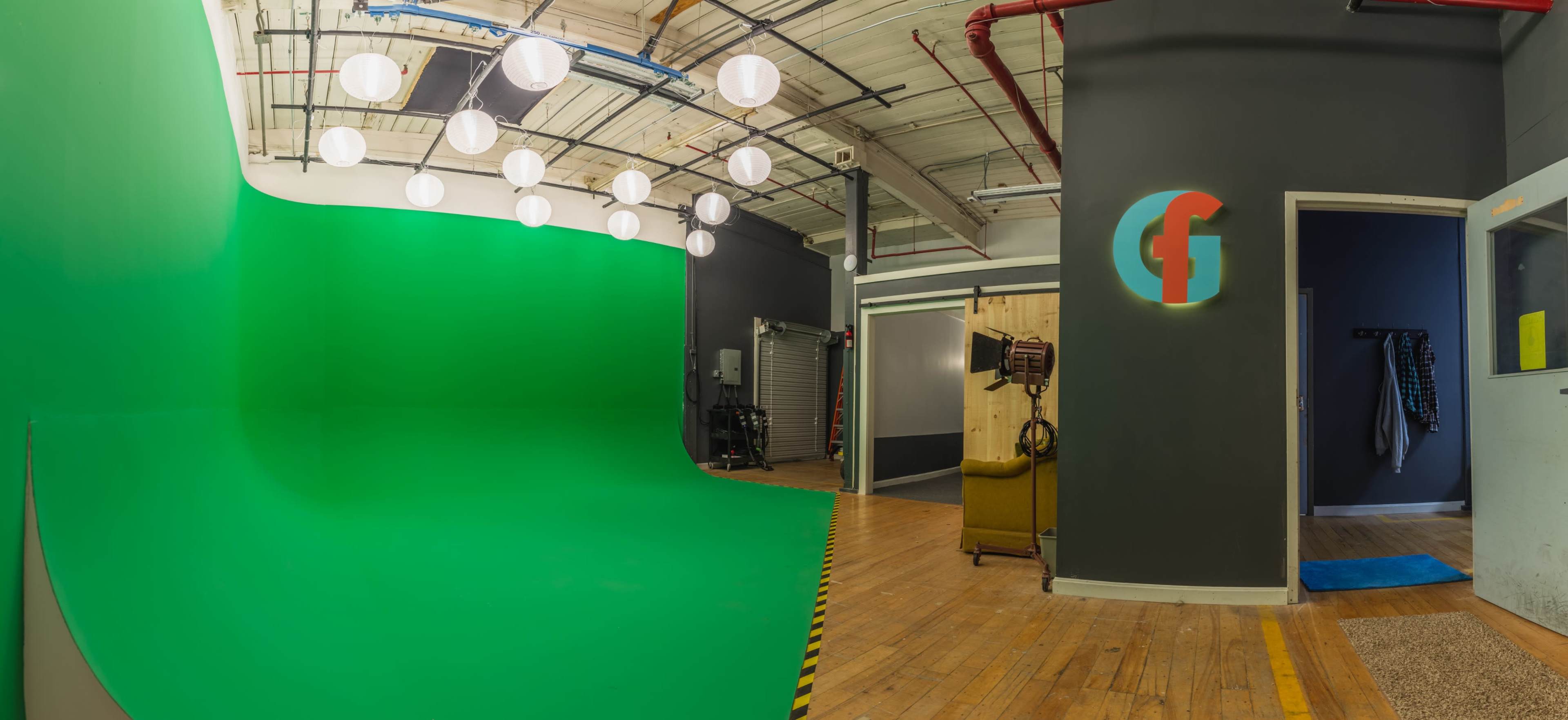 A studio with a green screen backdrop, overhead round lights, and an area with a visible logo on the wall.