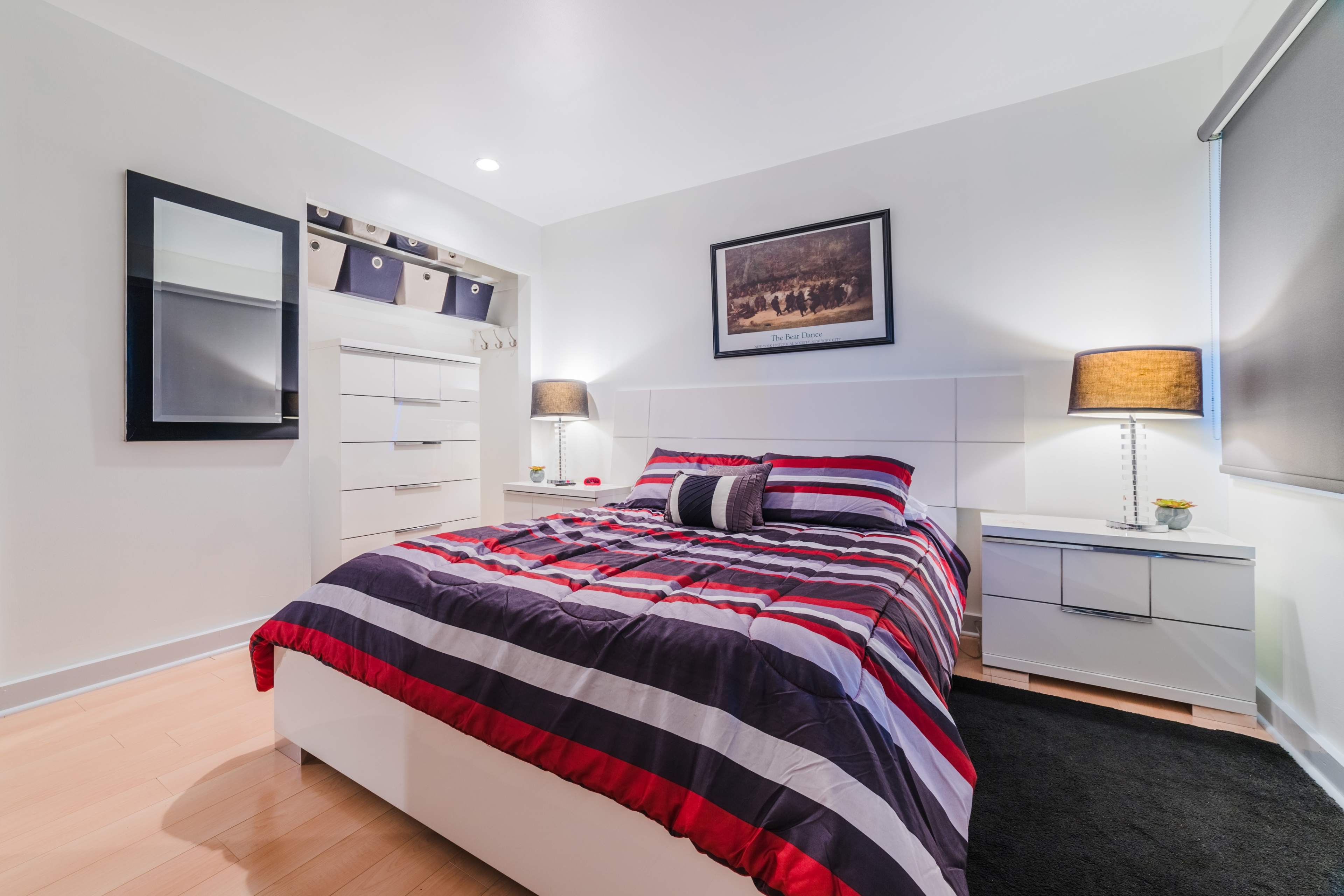 A modern bedroom featuring a striped bedspread, a white dresser, and two nightstands with lamps.