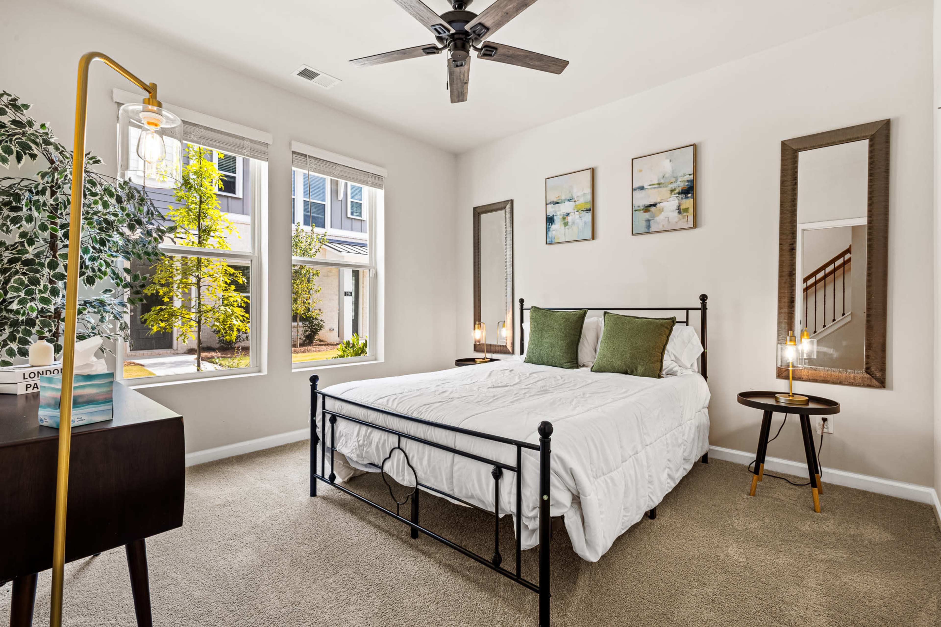 A neatly arranged bedroom features a bed with white bedding, two mirrors, and a window with natural light coming in.