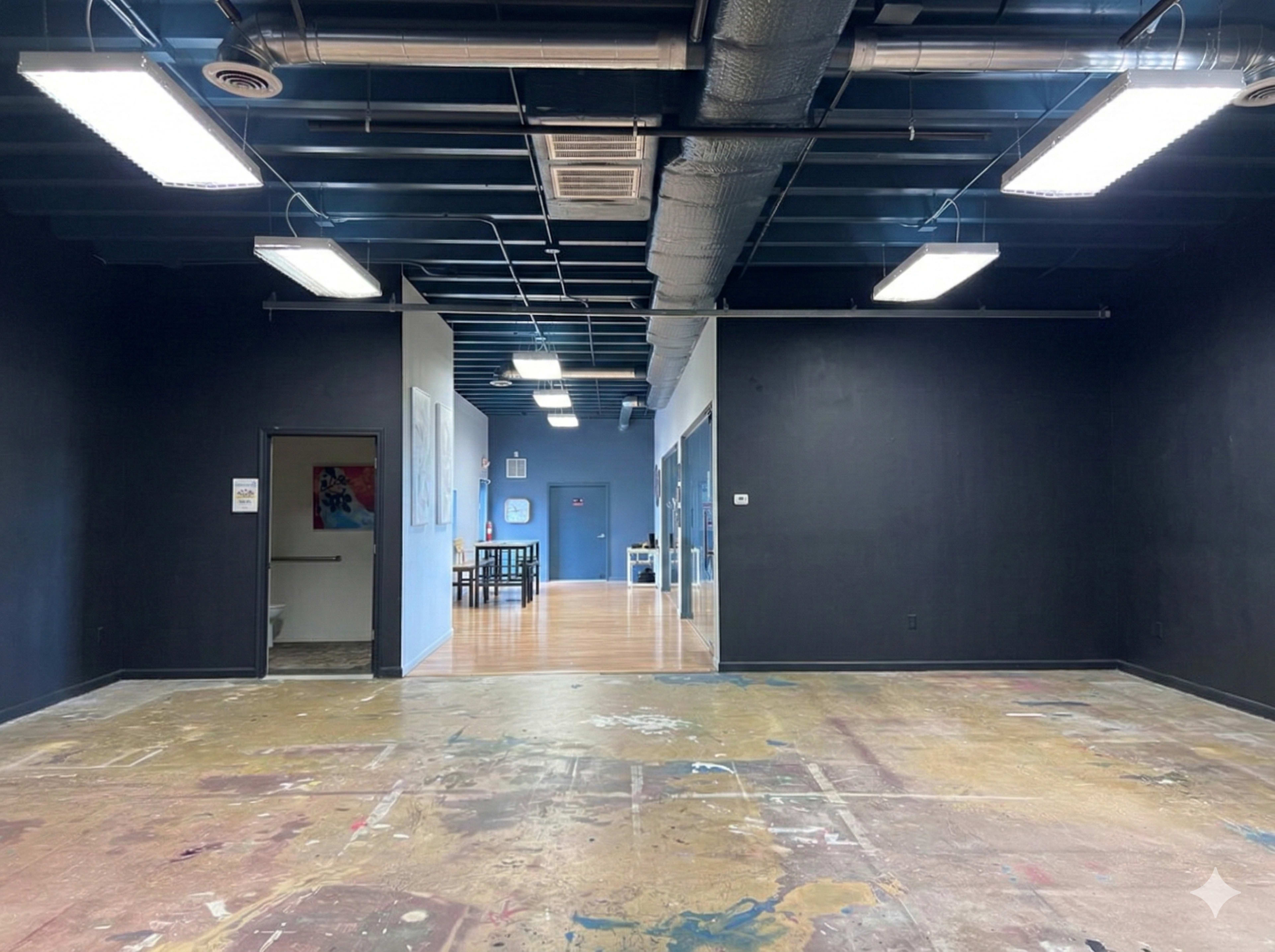 The image shows a spacious, partially painted room with a polished floor and two doorways leading to adjacent areas.