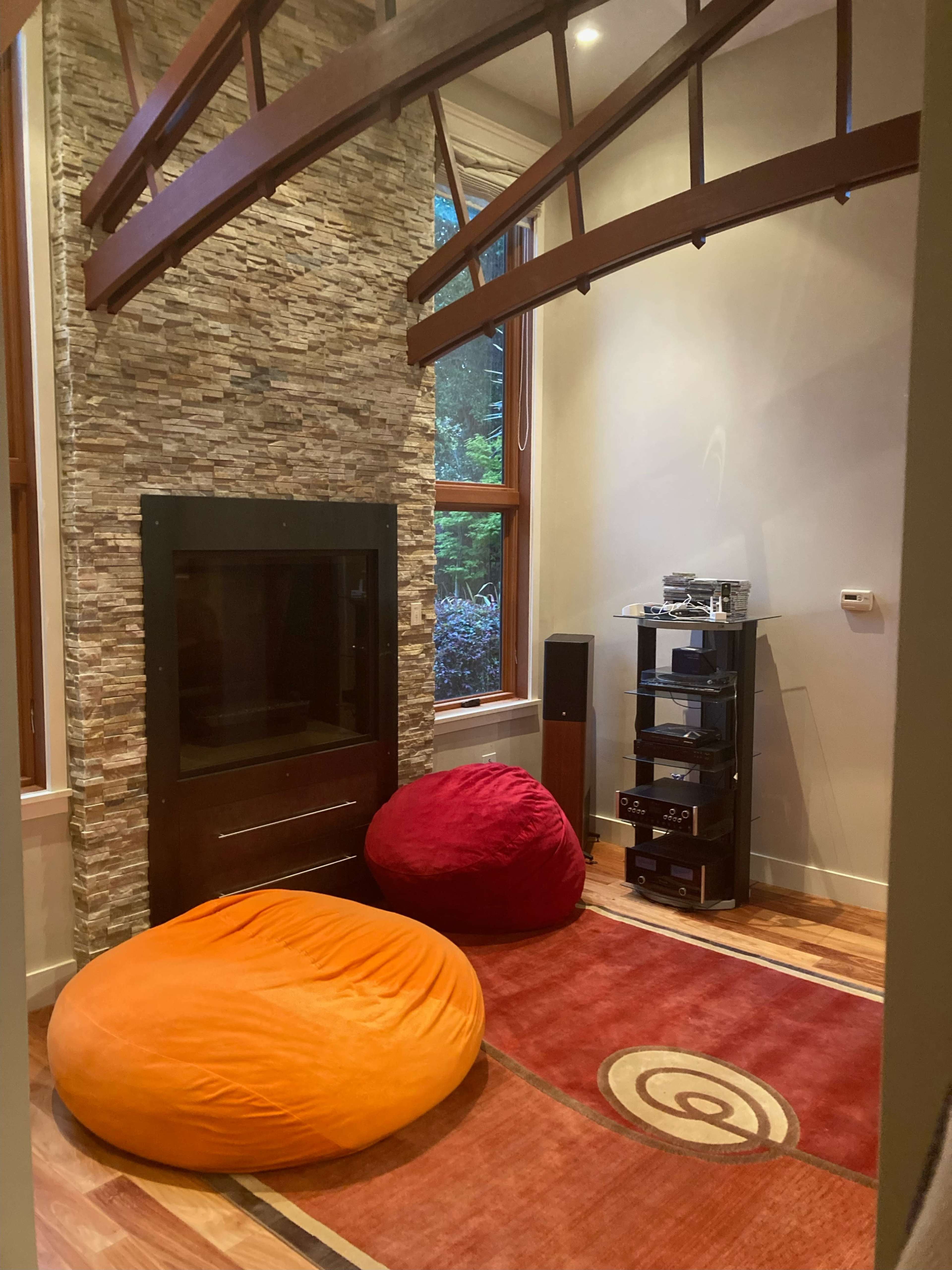 A cozy corner of a room featuring two large bean bags, a modern audio equipment stand, and a stone accent wall beneath a wooden beam structure.