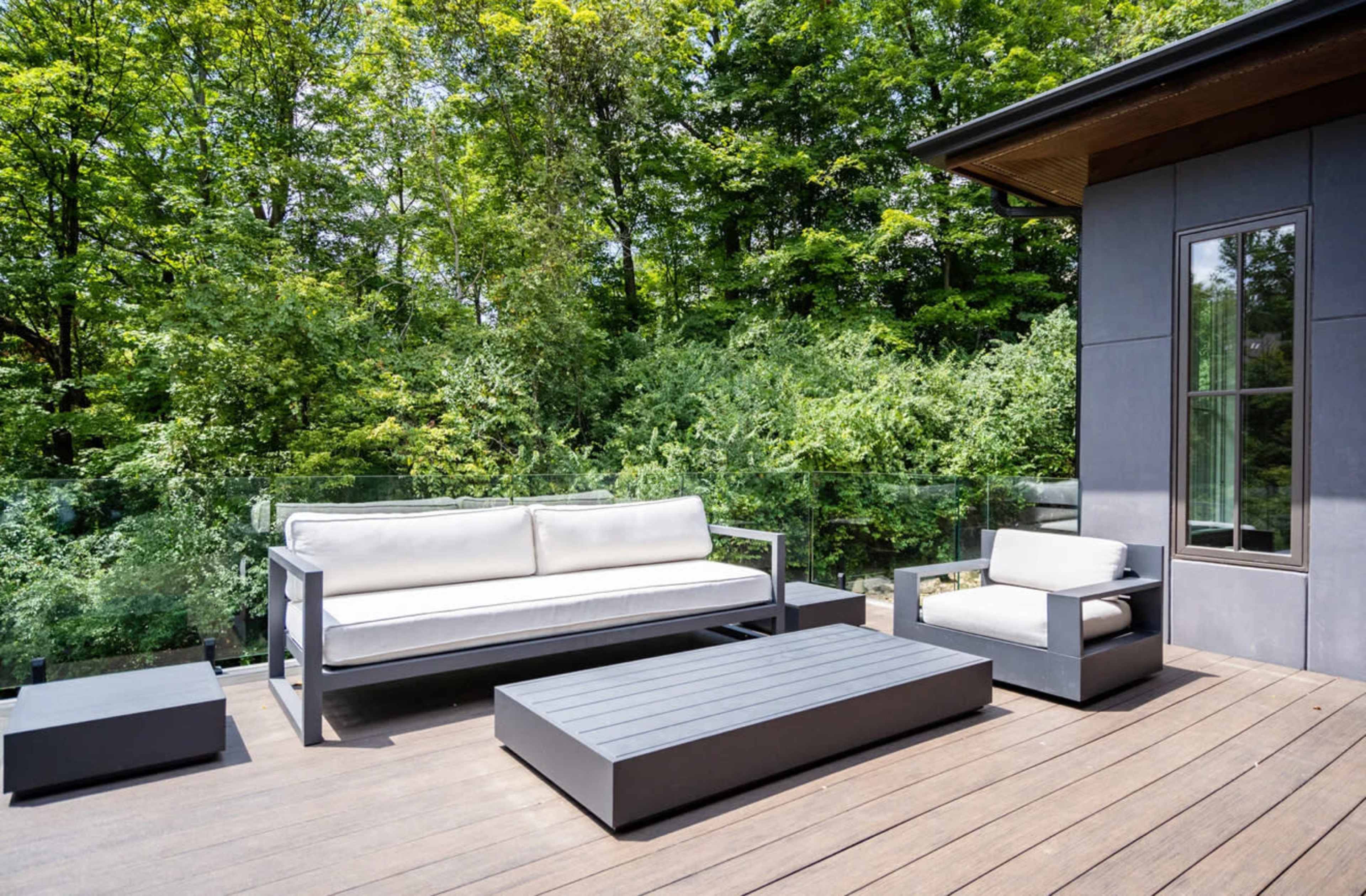 A modern patio features gray furniture, including a sofa and coffee table, surrounded by lush greenery.