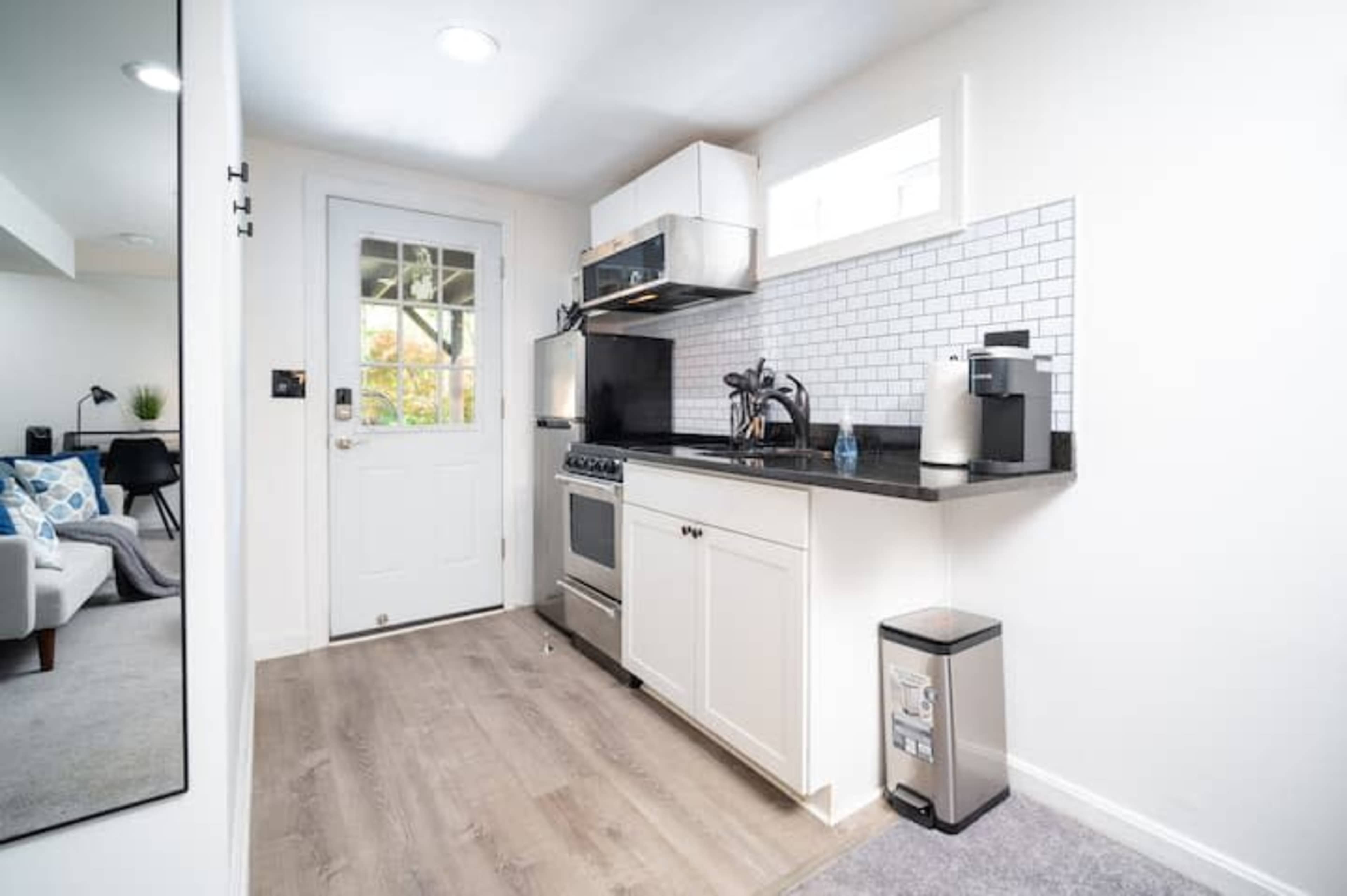 A modern kitchen with white cabinetry, a stainless steel oven, and a door leading outside.