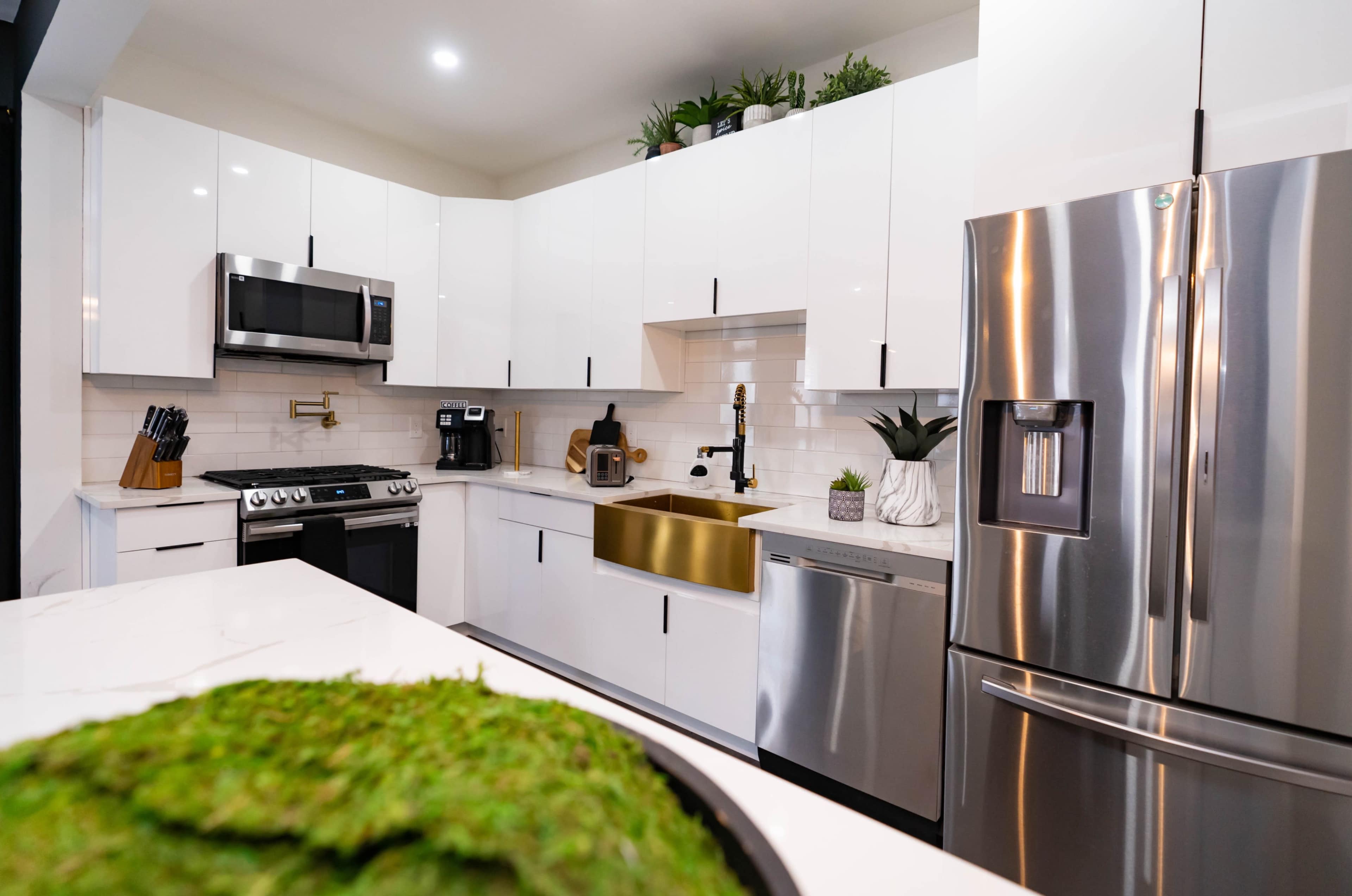 A modern kitchen features stainless steel appliances, white cabinetry, and a gold sink.