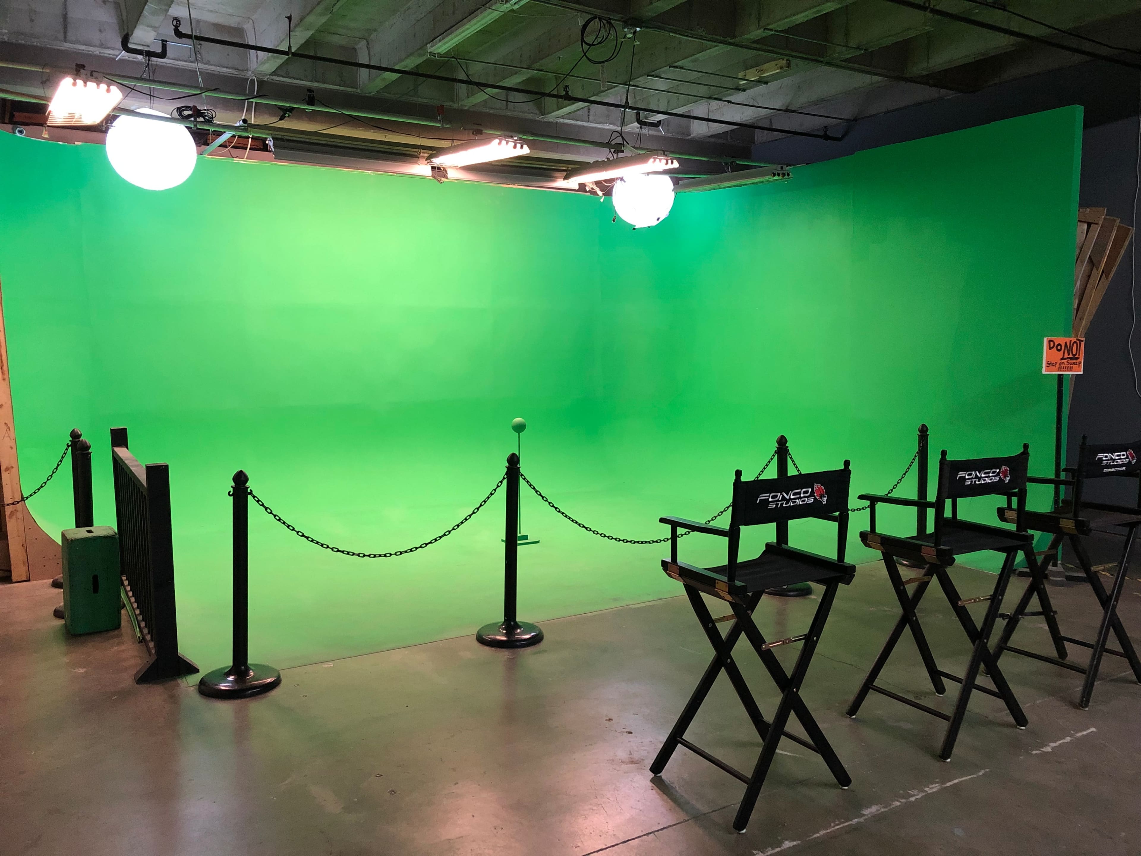 A studio space with a bright green backdrop, director's chairs, and overhead lighting.