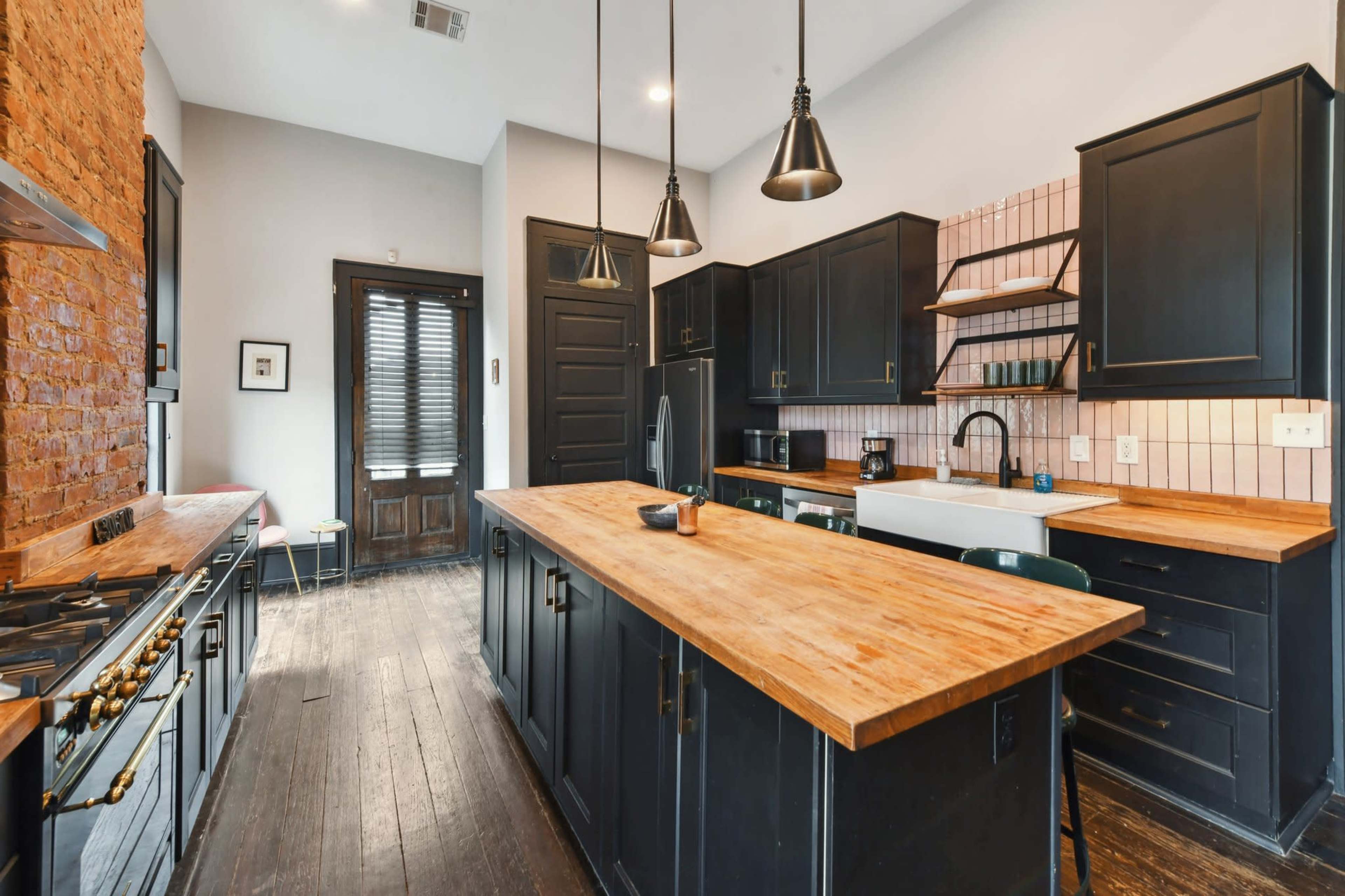 The kitchen features dark cabinetry with wooden countertops, a large sink, and brick accents on the wall.