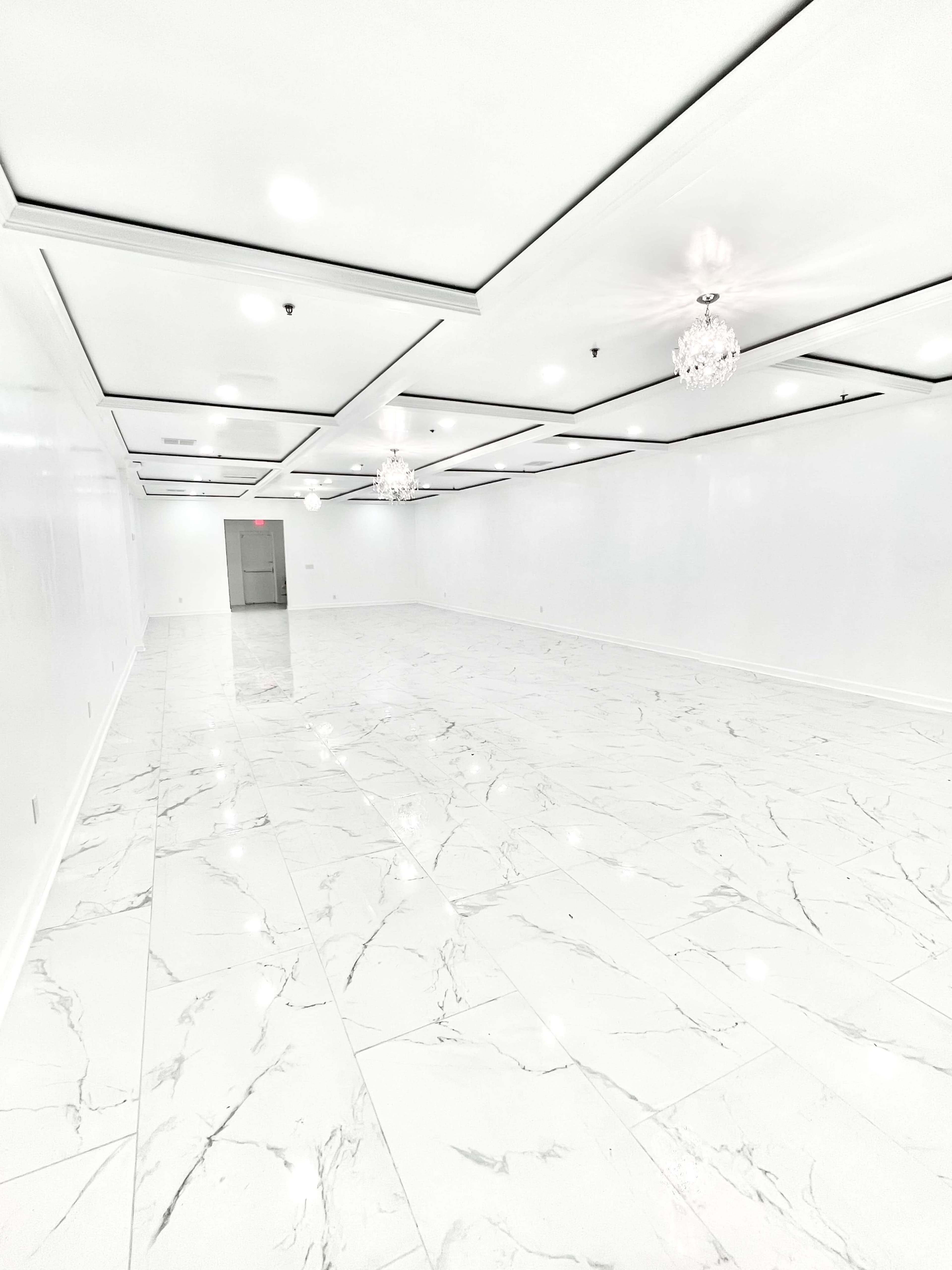 A spacious, empty room with white marble flooring and modern ceiling fixtures.