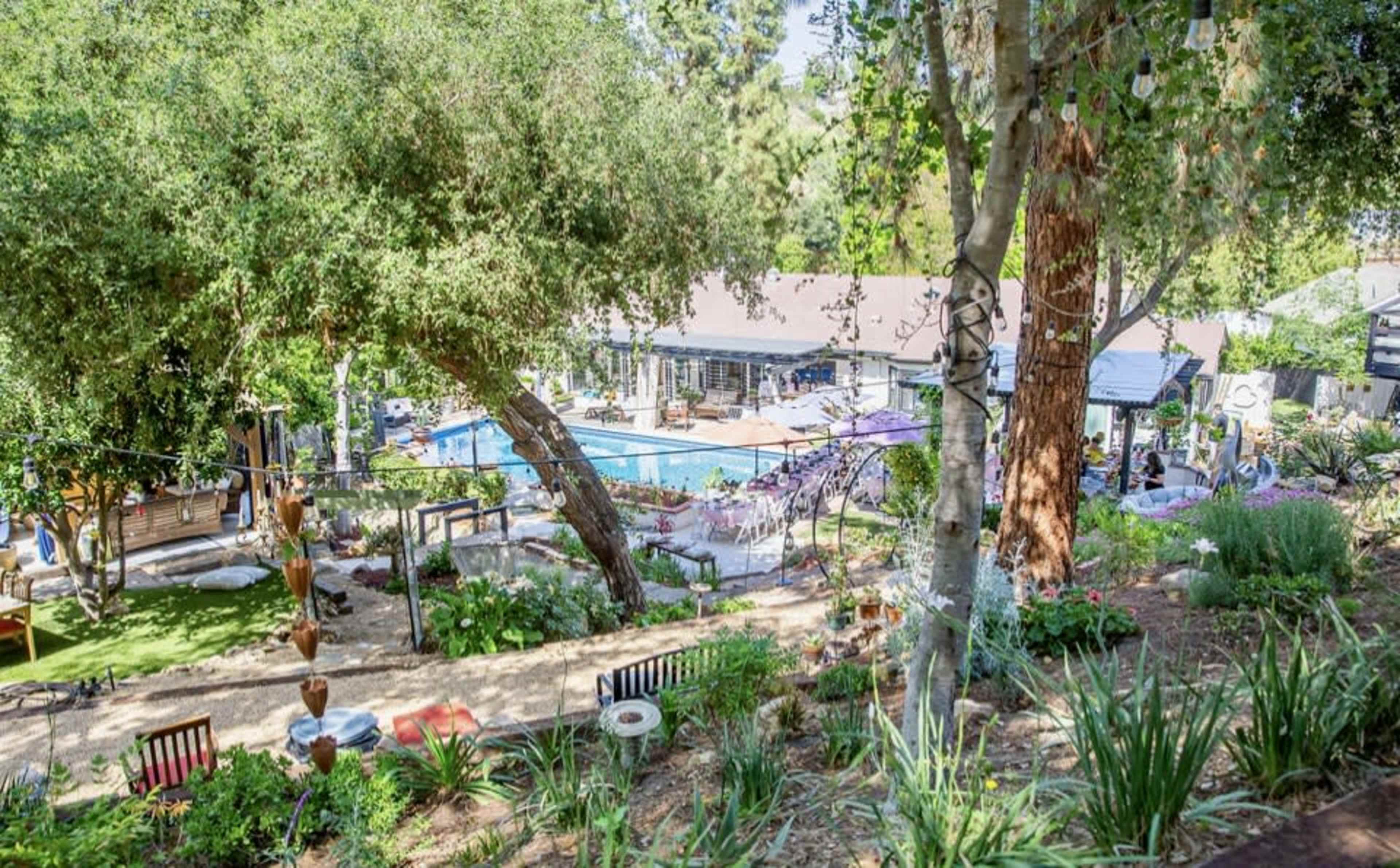A landscaped outdoor area features a swimming pool surrounded by lounge chairs, trees, and gardens, with a gathering space above.