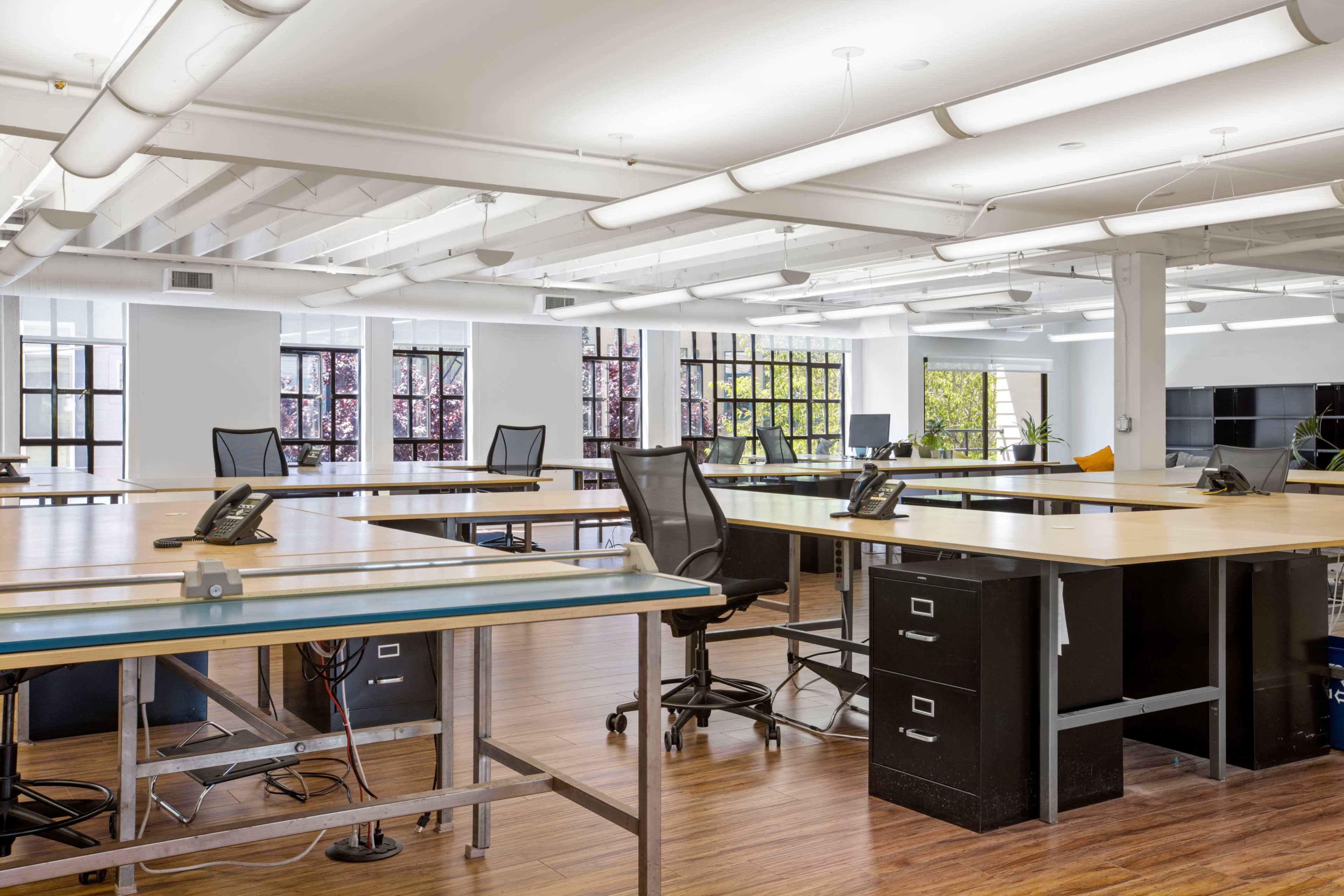 A spacious, modern office environment with multiple workstations featuring desks, chairs, and phones, and large windows allowing natural light.