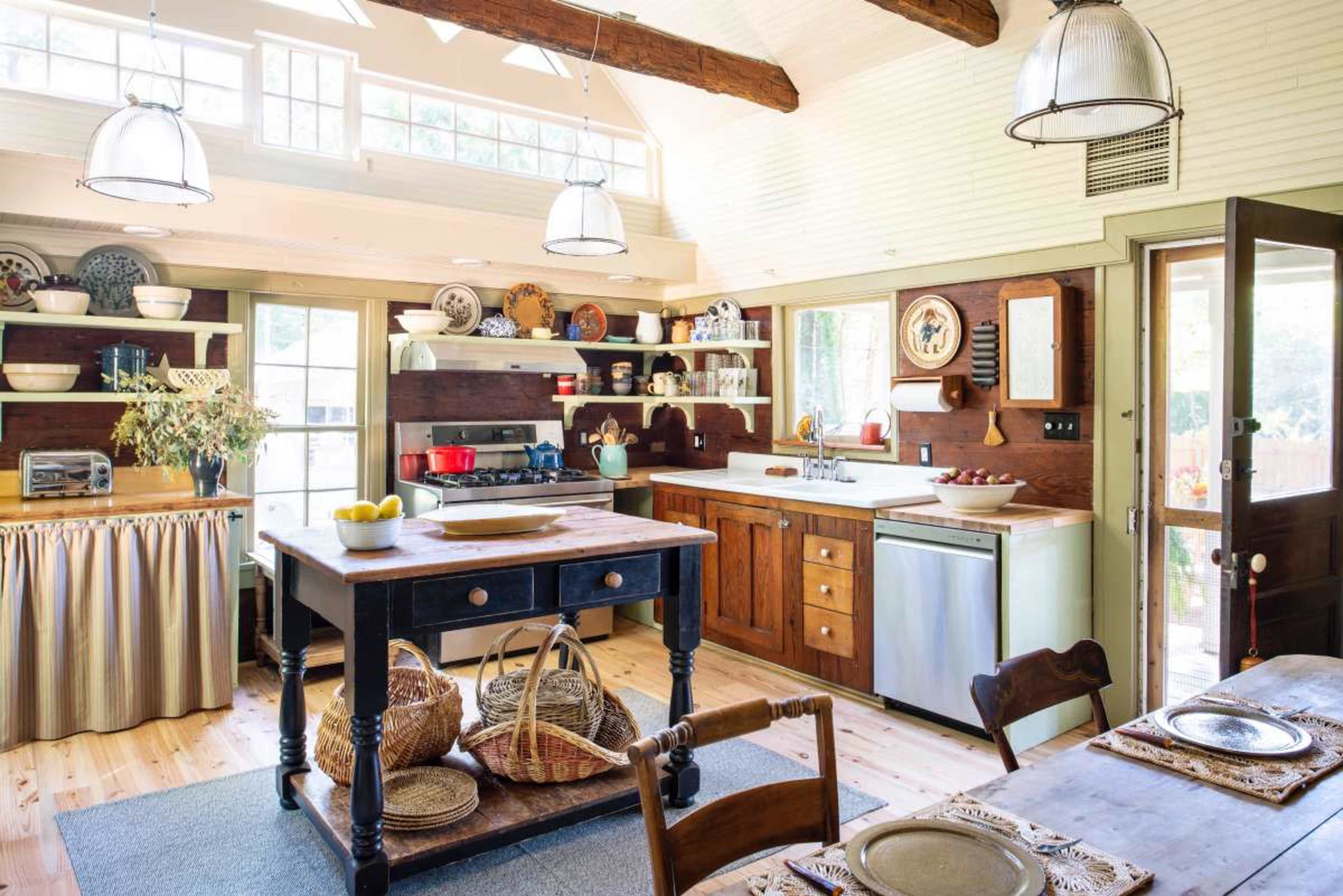 A rustic kitchen features wooden beams, an island with storage, and shelves displaying dishes and cookware.