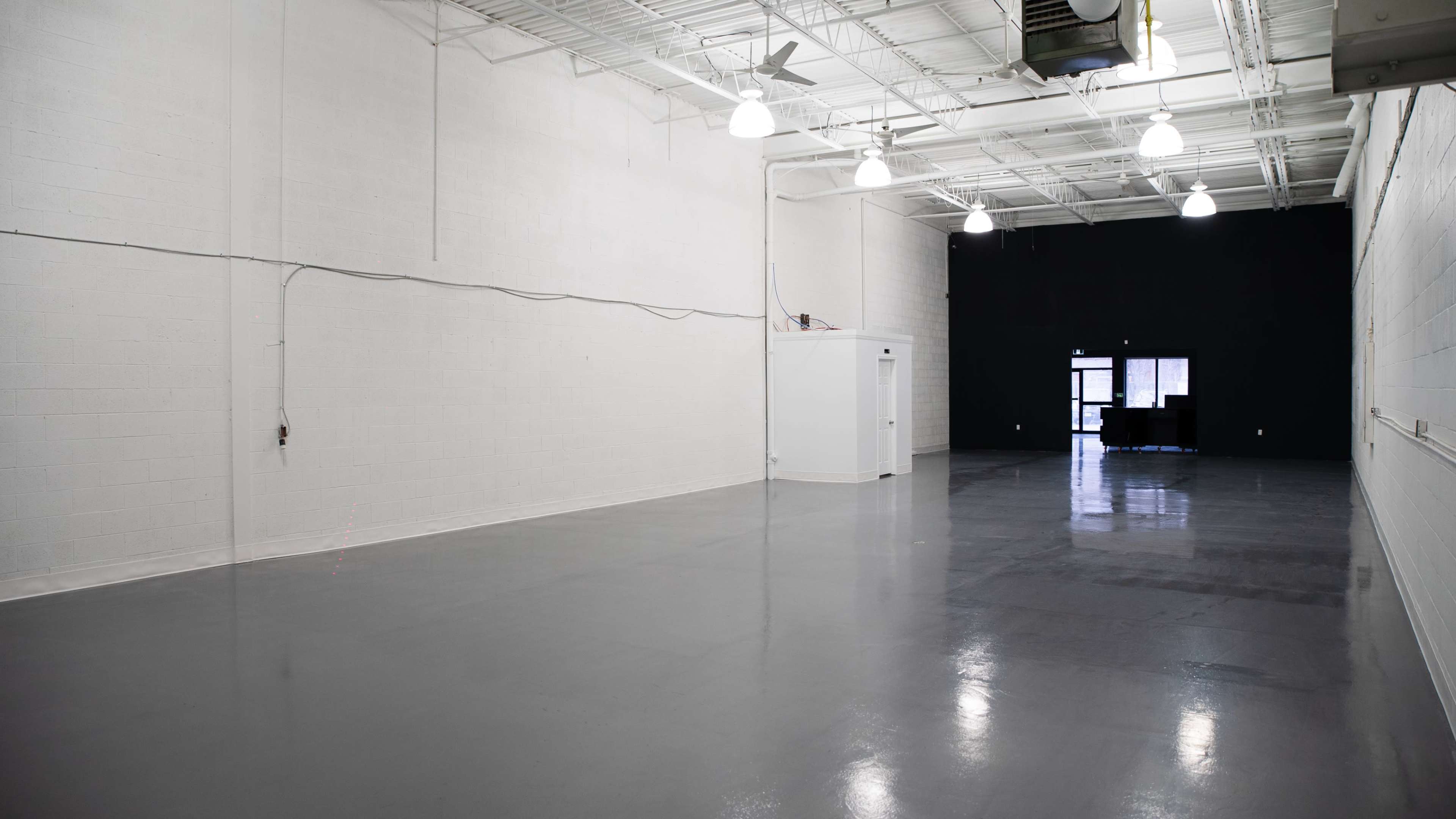 An empty, spacious room with a polished gray floor, white walls, and a contrasting black wall at one end.