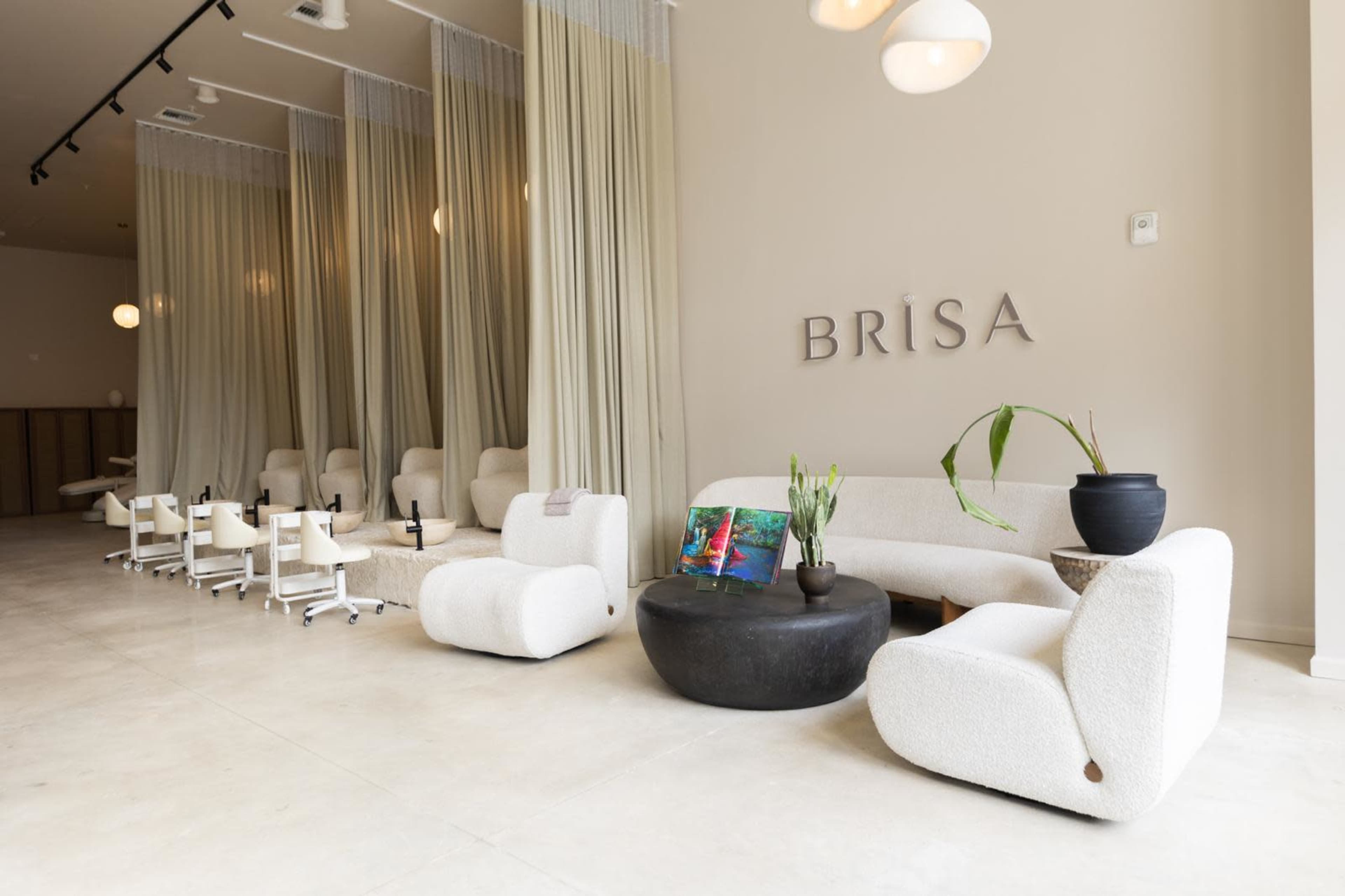 The image shows a modern salon interior featuring soft, rounded furniture, with multiple workstations separated by sheer curtains, and a large sign that reads "BRISA" on the wall.