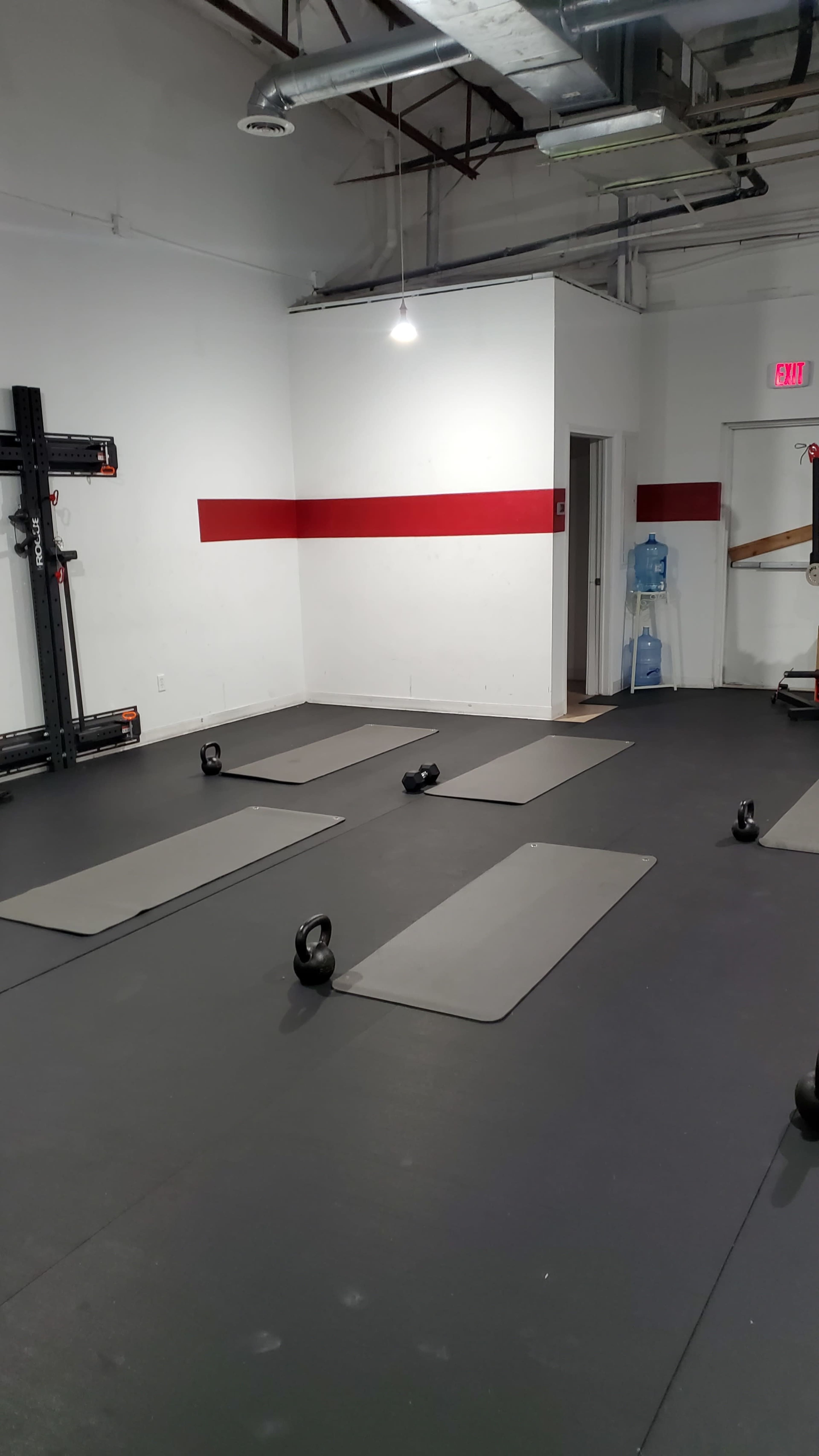 A workout space with several exercise mats laid out on a black floor, kettlebells placed on each mat, and a wall with a red stripe.