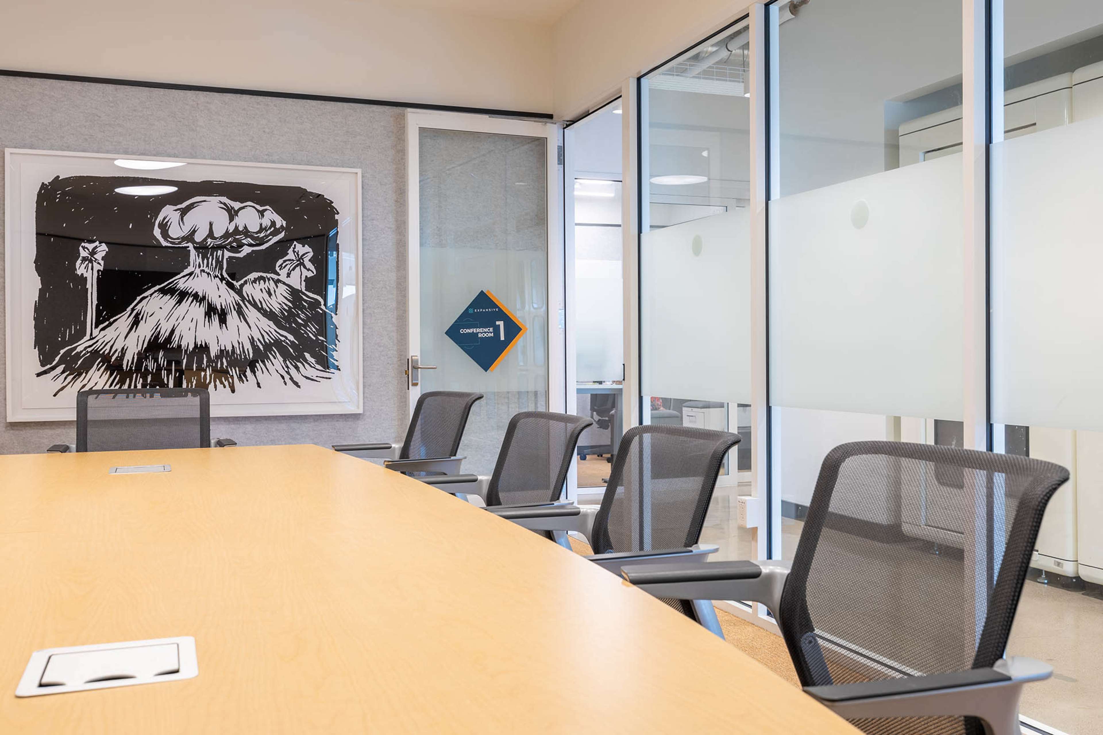 The image shows a modern conference room with a large wooden table, mesh chairs, and an illustration of a volcano on the wall.