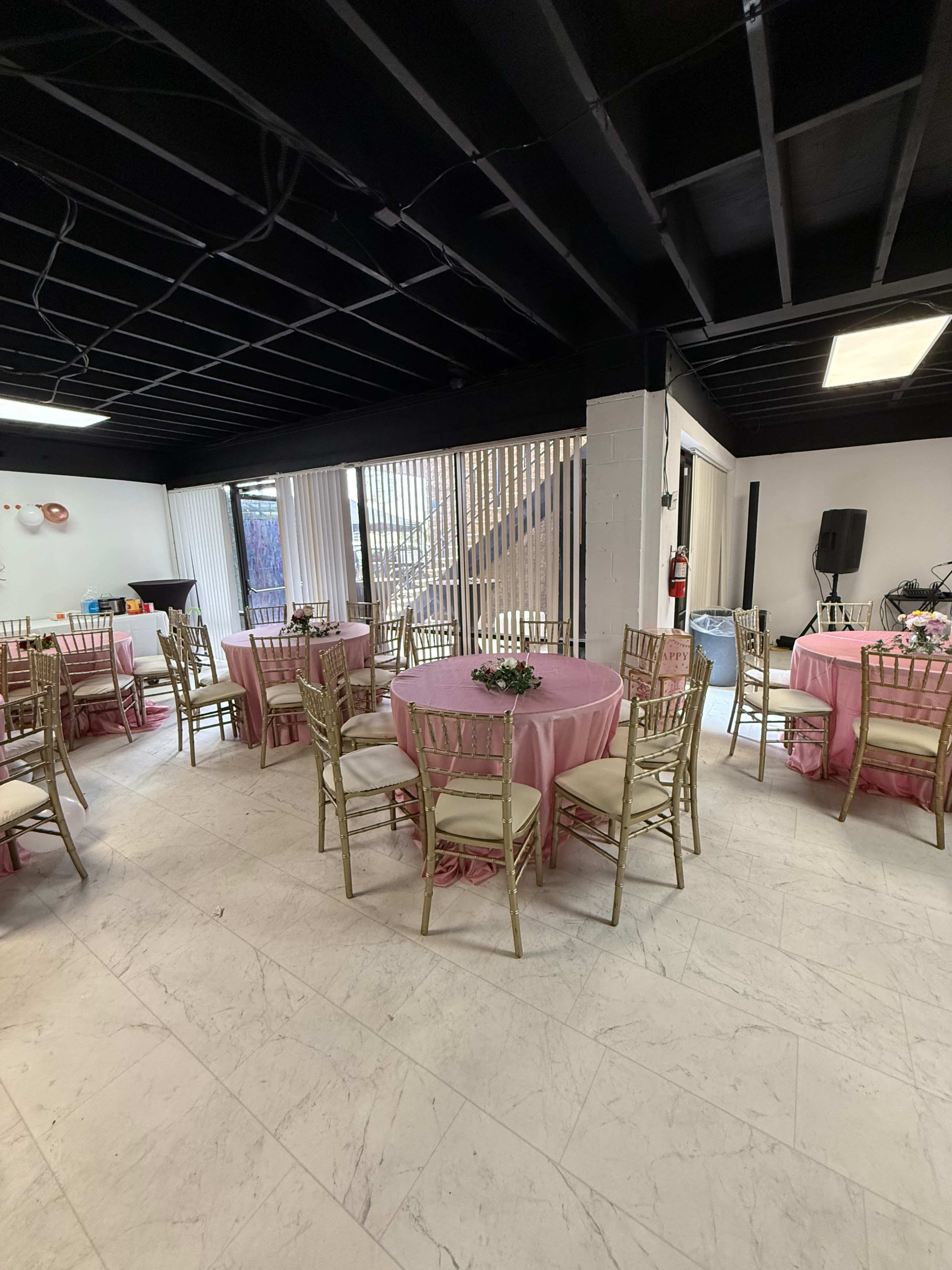 The image shows a banquet room with circular tables covered in pink tablecloths, surrounded by gold chairs, and decorated with floral centerpieces.