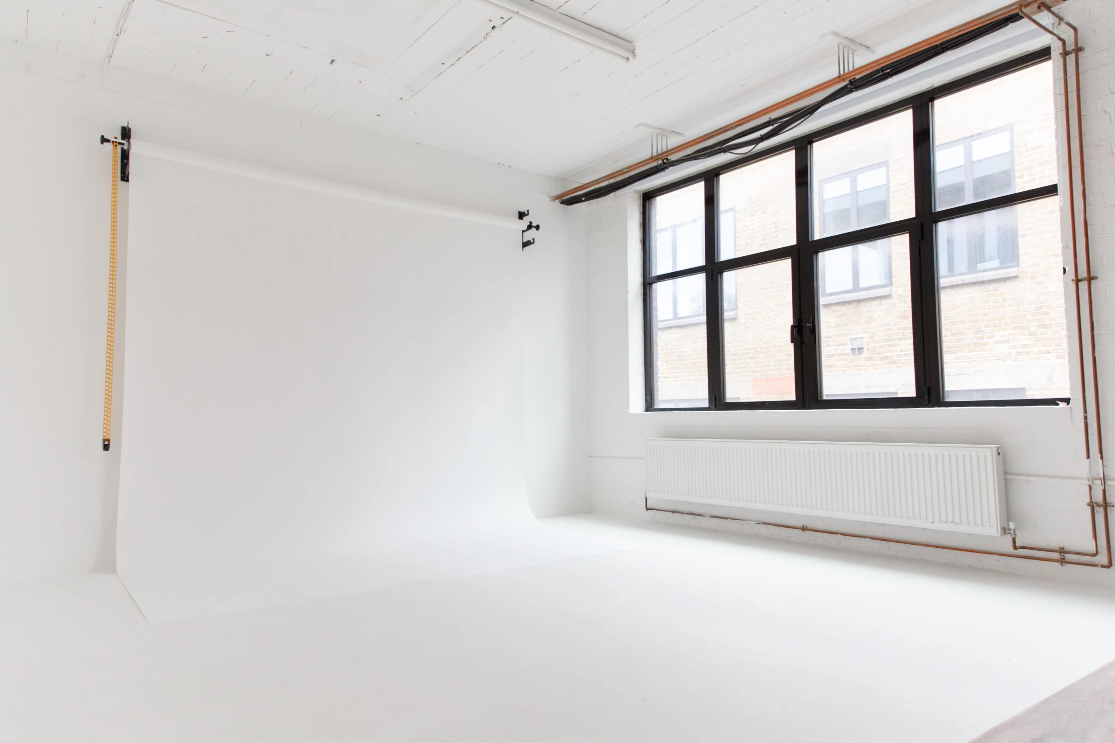 A bright, empty photography studio with a white backdrop and large windows letting in natural light.