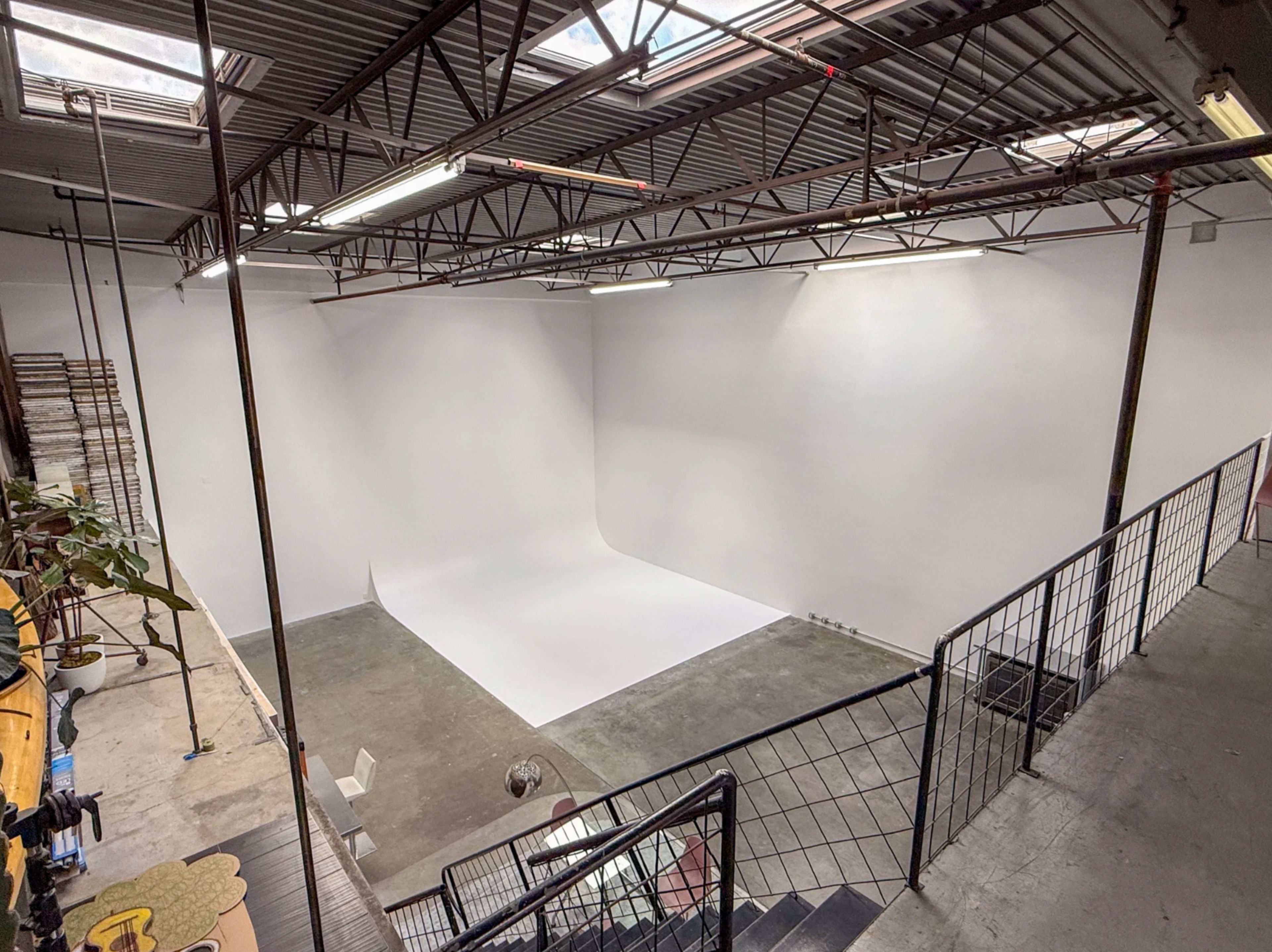 The image shows a spacious photography studio with white walls and a large white backdrop, illuminated by overhead lights.
