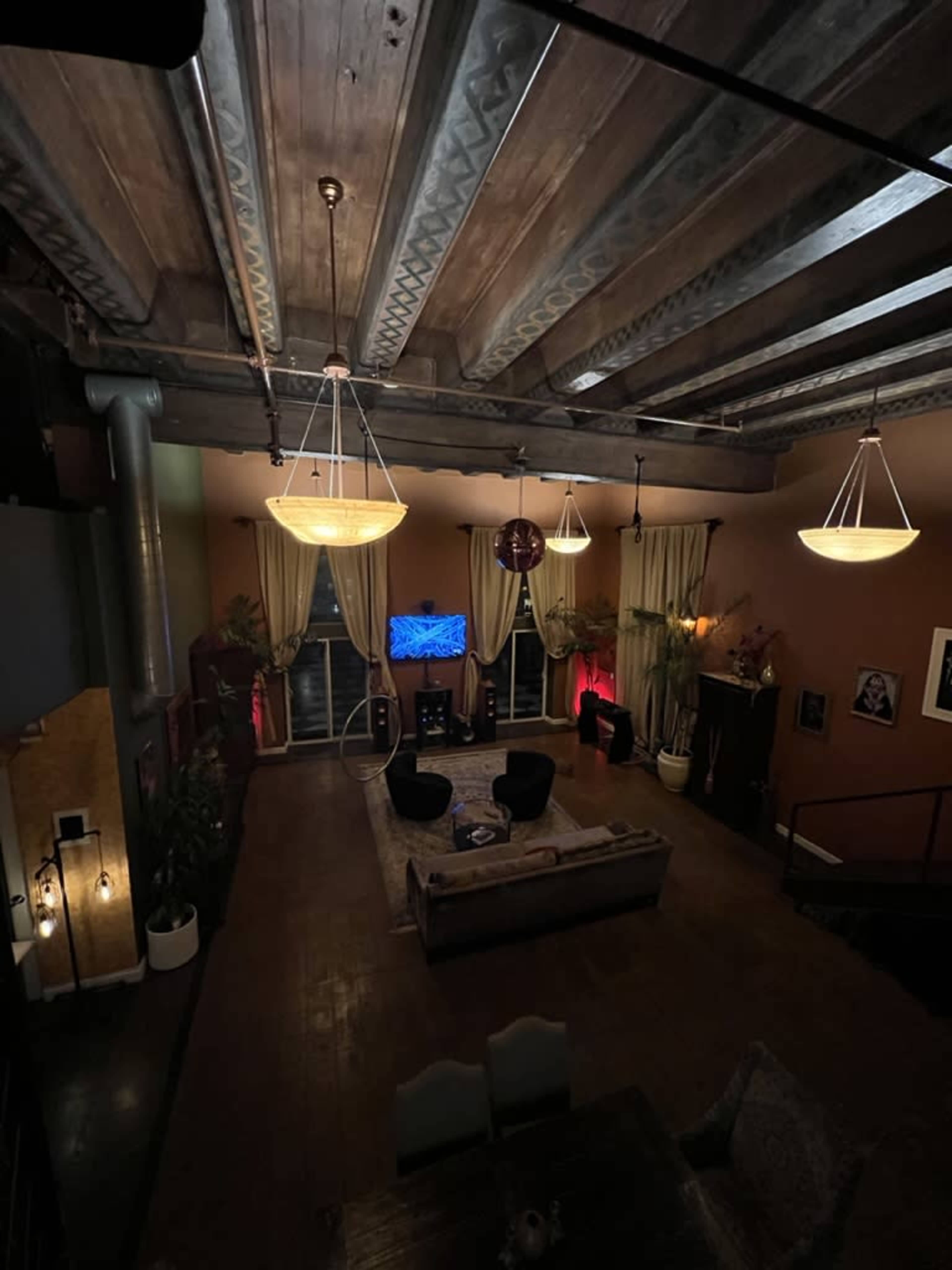 A spacious living room with wooden beams on the ceiling, a television mounted on the wall, and a cozy seating arrangement around a central coffee table.