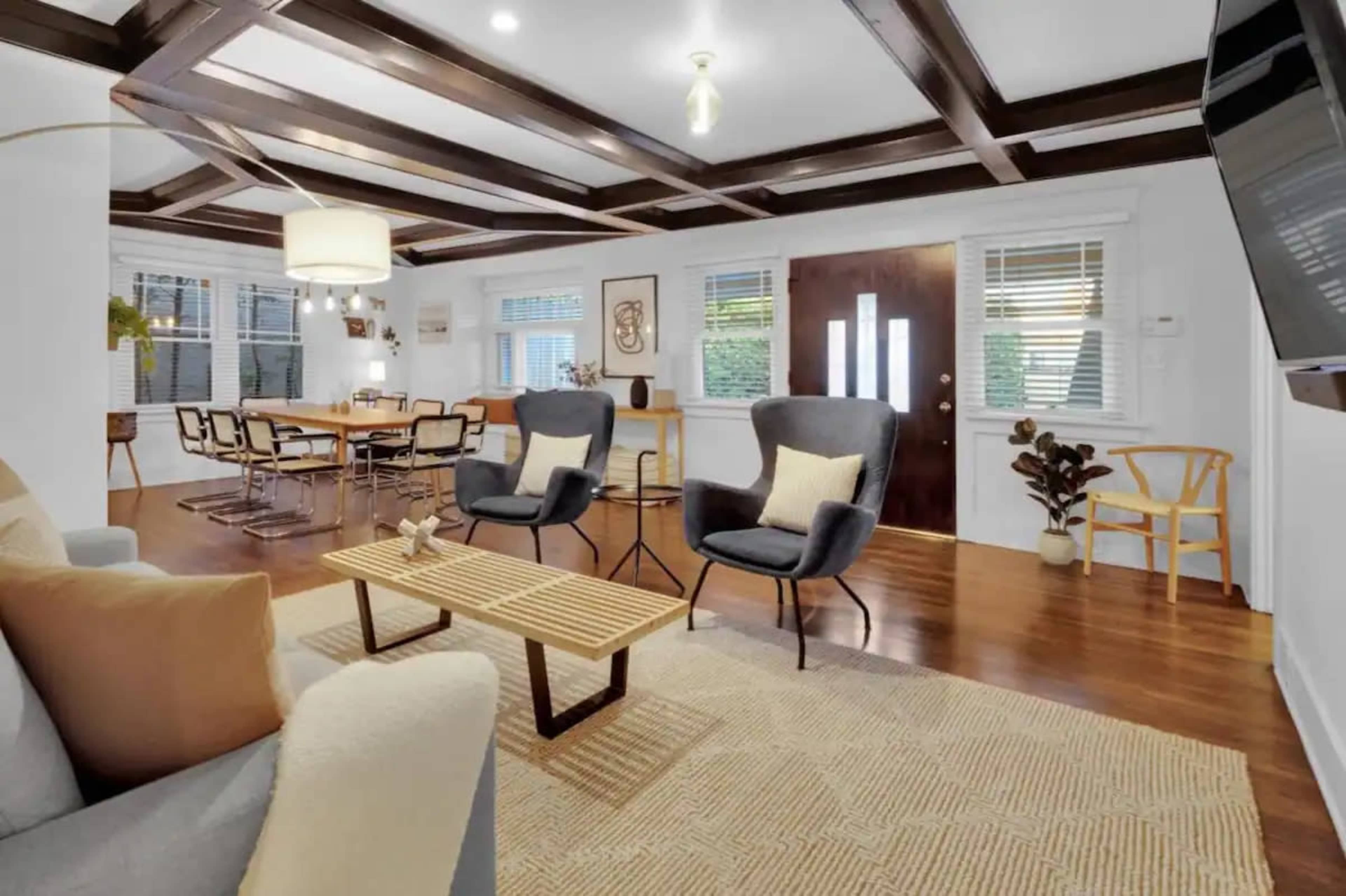 A modern living room features two armchairs facing a coffee table, with a dining area visible in the background, all under a coffered ceiling.