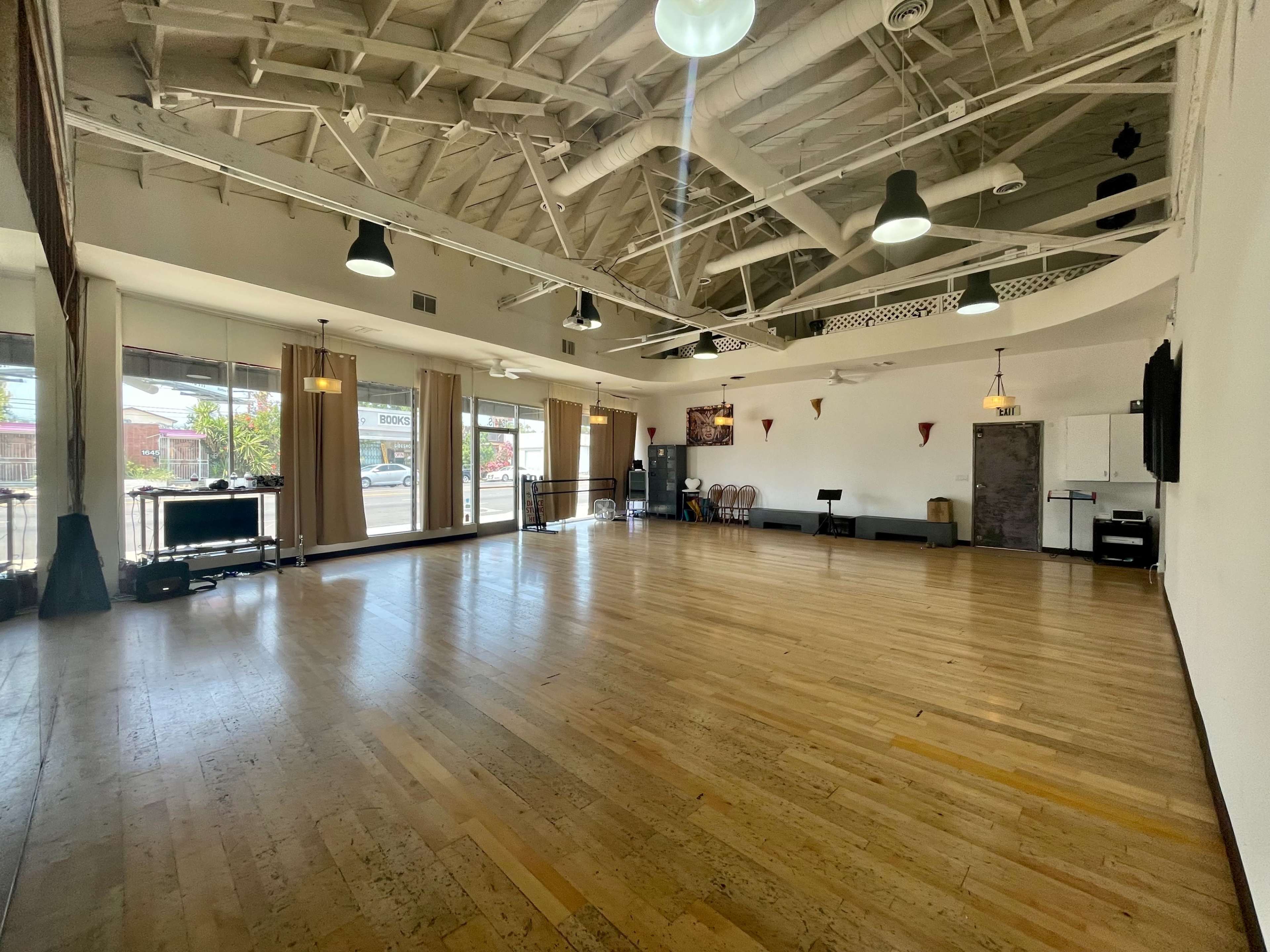 The image shows a spacious, well-lit interior of a dance studio with wooden flooring and large windows.