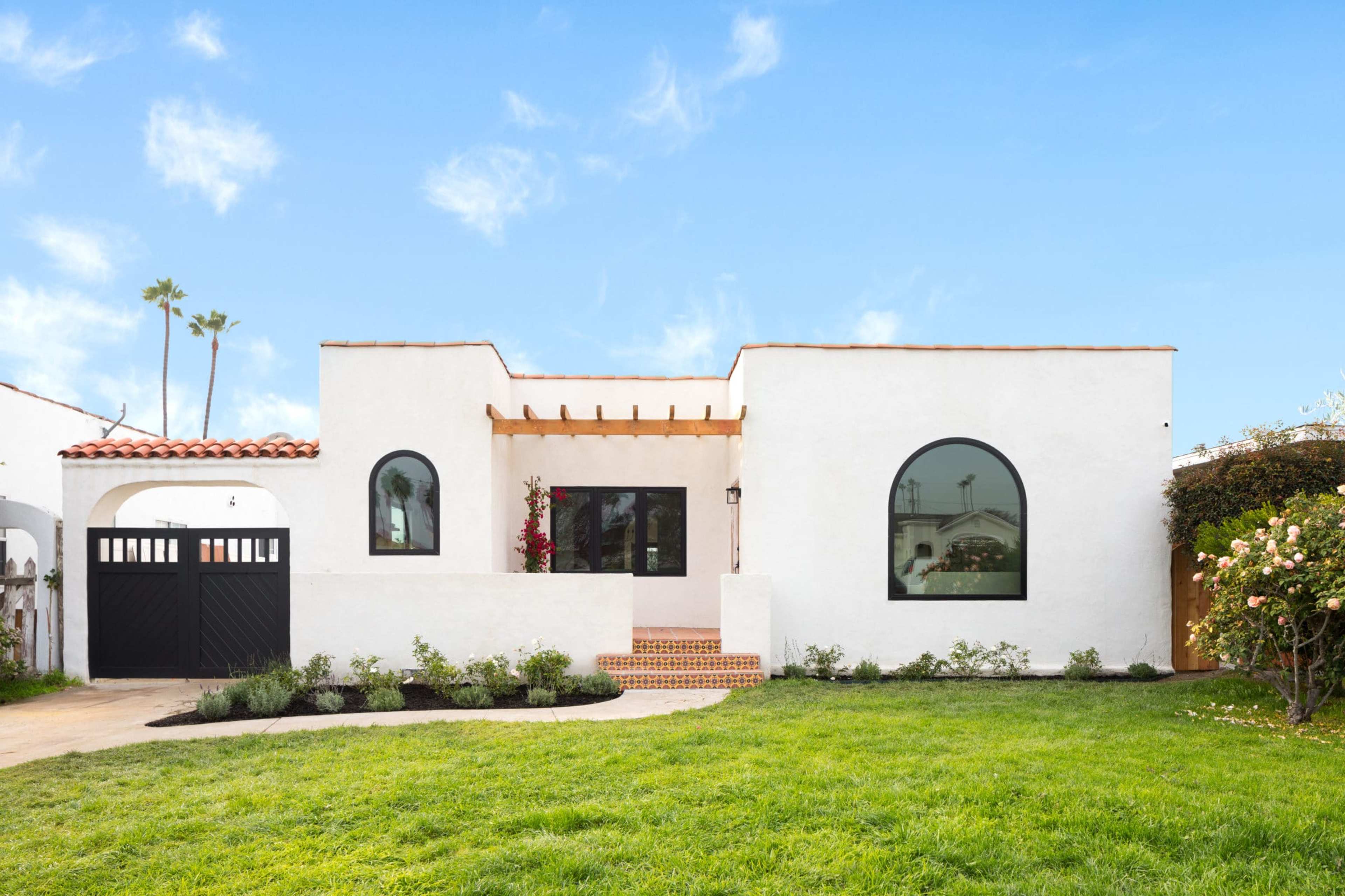 A white stucco house with arched windows, a tiled roof, and a landscaped front yard.
