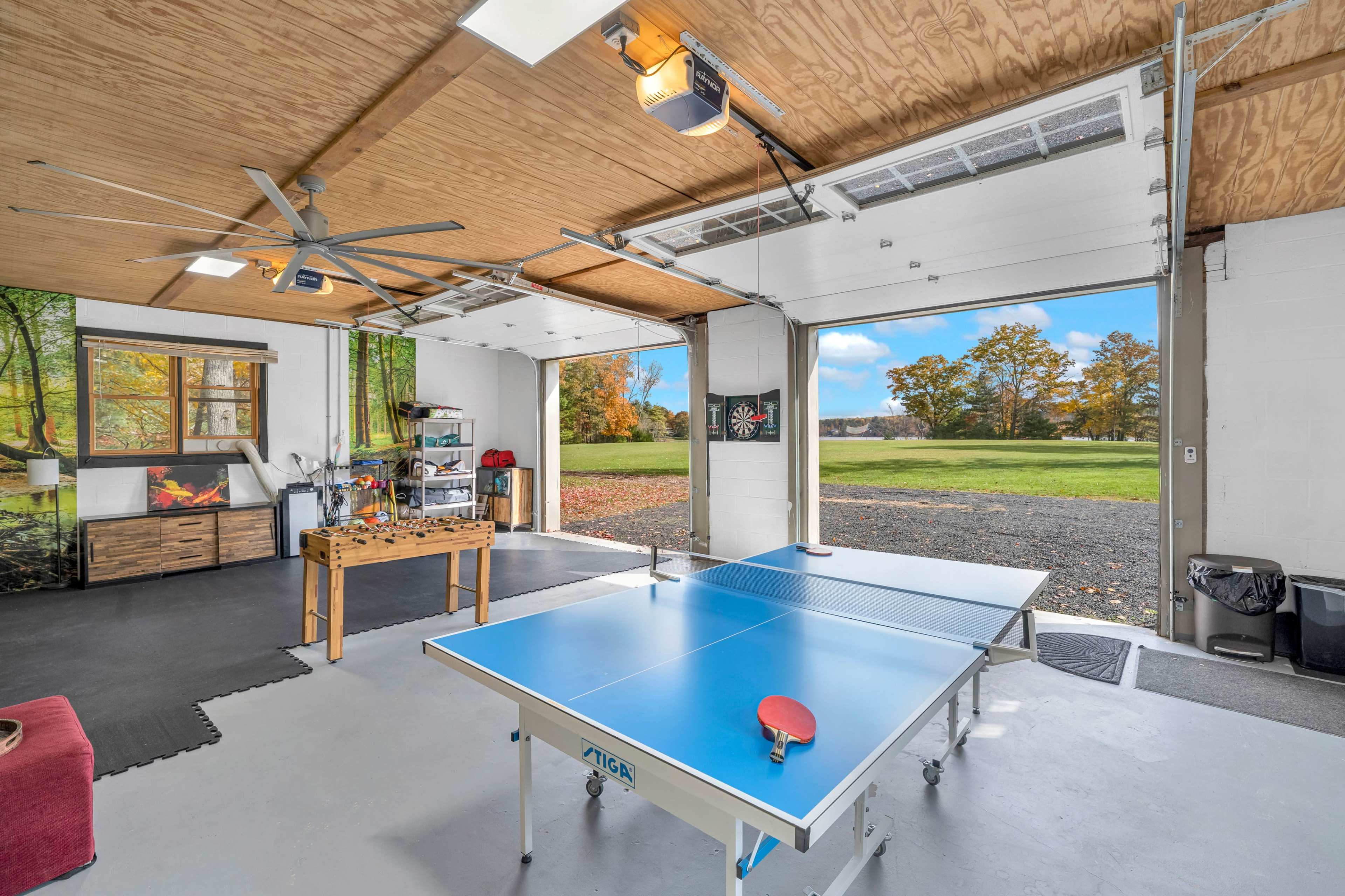 A bright garage features an open design with a ping pong table in the center and large doors leading to an outdoor view.