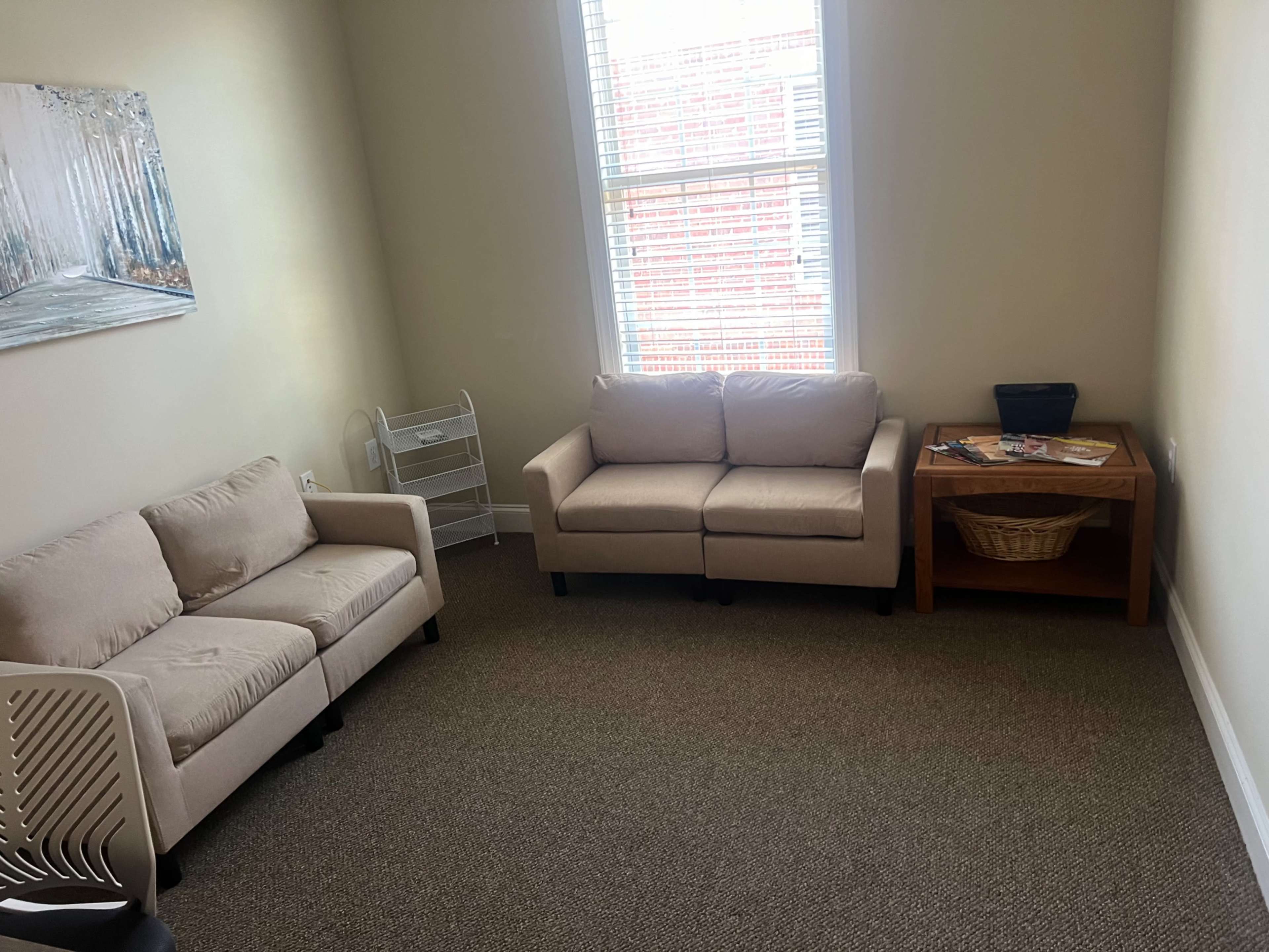 The image shows a small room with two beige sofas, a wooden table with a basket, and a window letting in natural light.