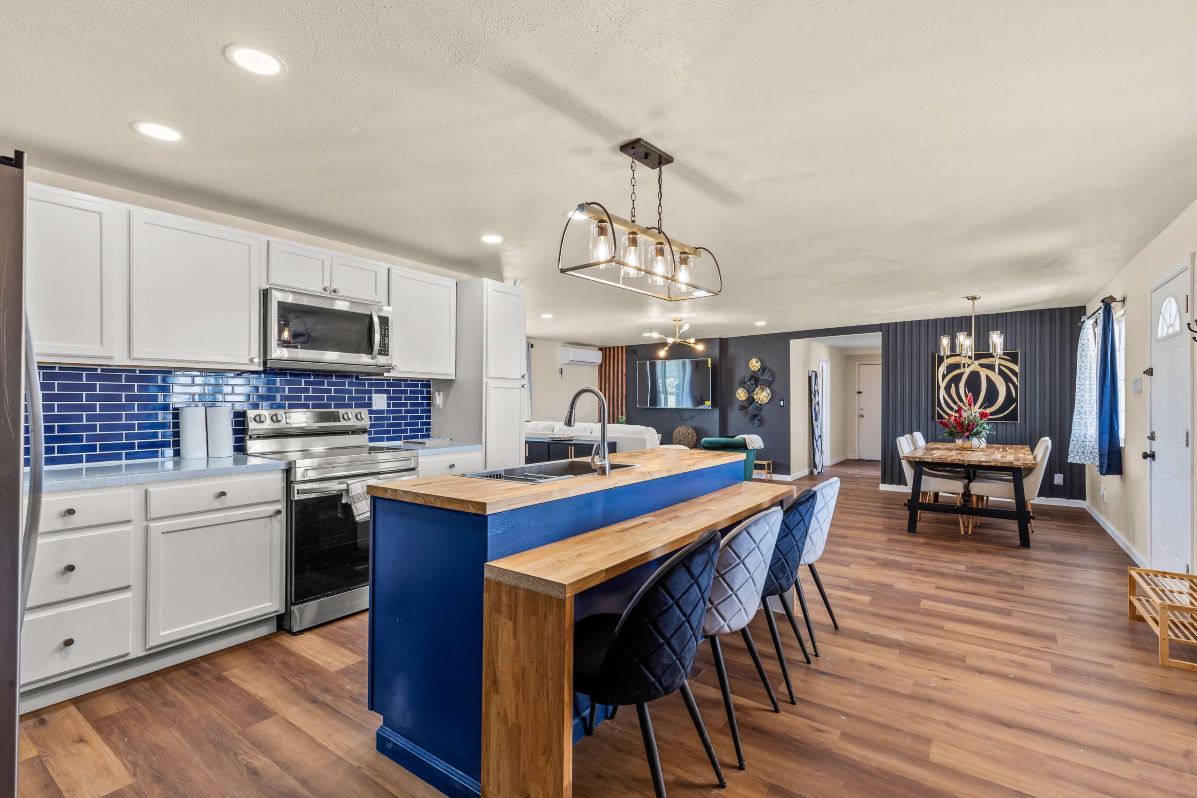 A modern kitchen with a blue and white color scheme, featuring a large island with bar seating, stainless steel appliances, and an adjacent dining area.