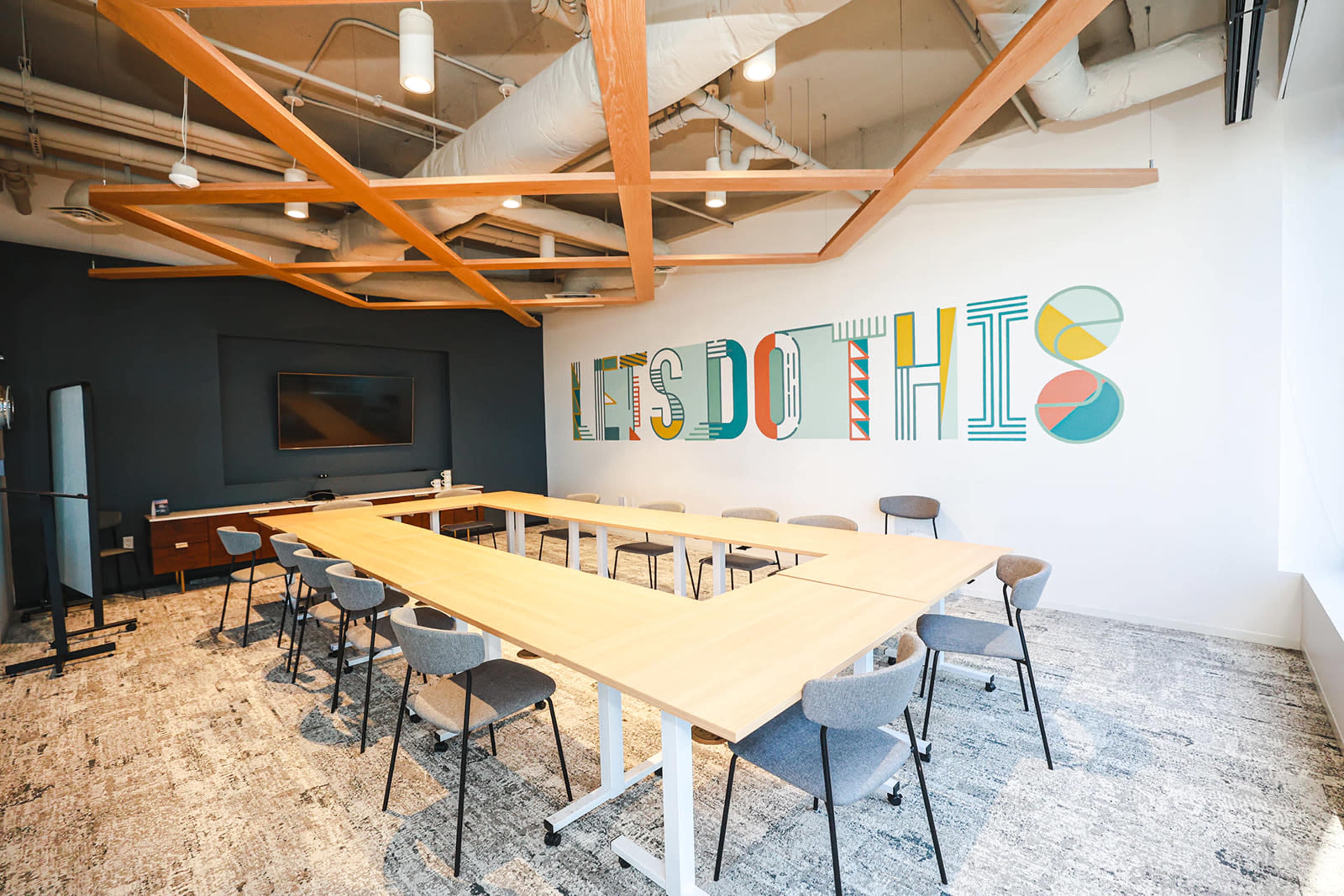 The image shows a modern conference room with a long table, multiple chairs, and a wall featuring colorful text that reads "LET'S DO THIS."