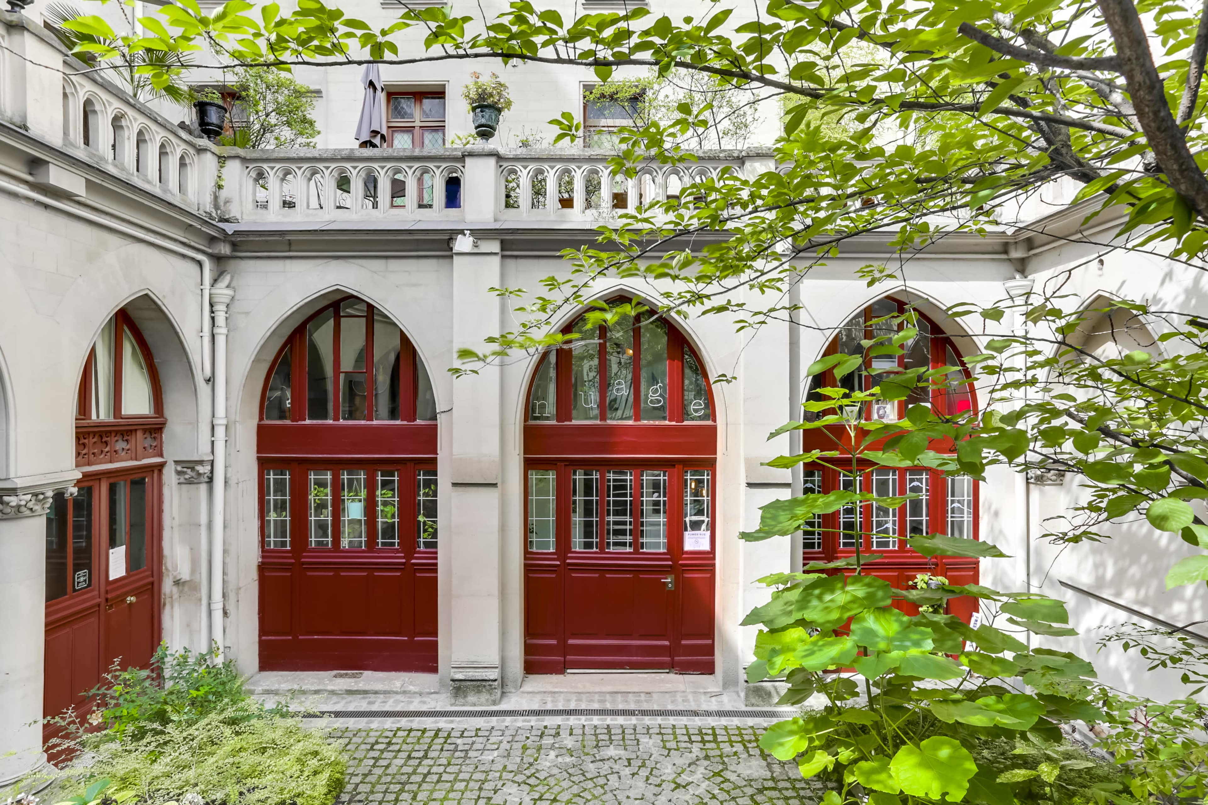 A courtyard with three arched red doors surrounded by gray stone walls and greenery.