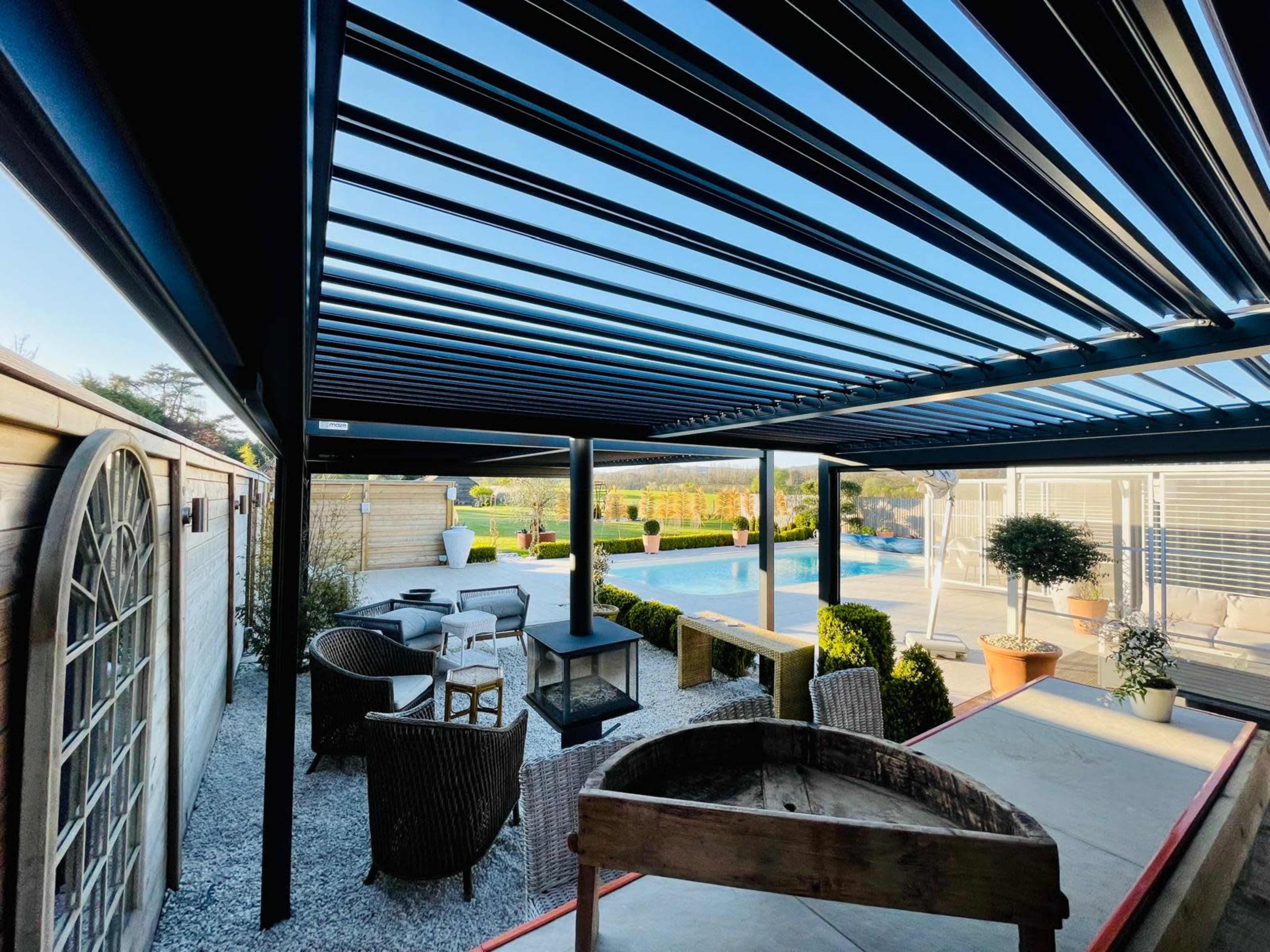 The image shows a modern outdoor patio area featuring a pergola, a dining table, seating arrangements, and a pool in the background.