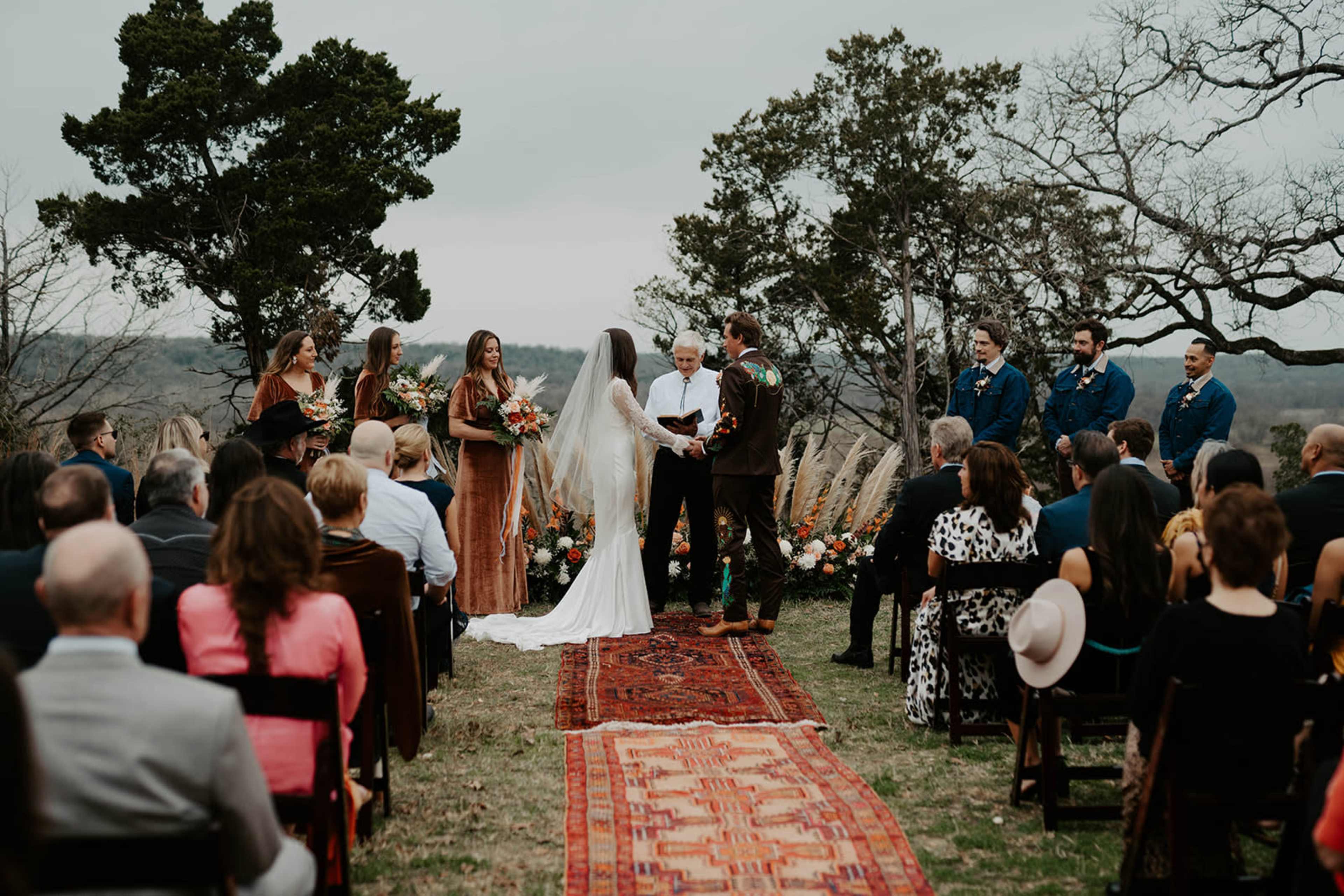 A couple exchanges vows during an outdoor wedding ceremony attended by friends and family, with a decorated altar and scenic backdrop.