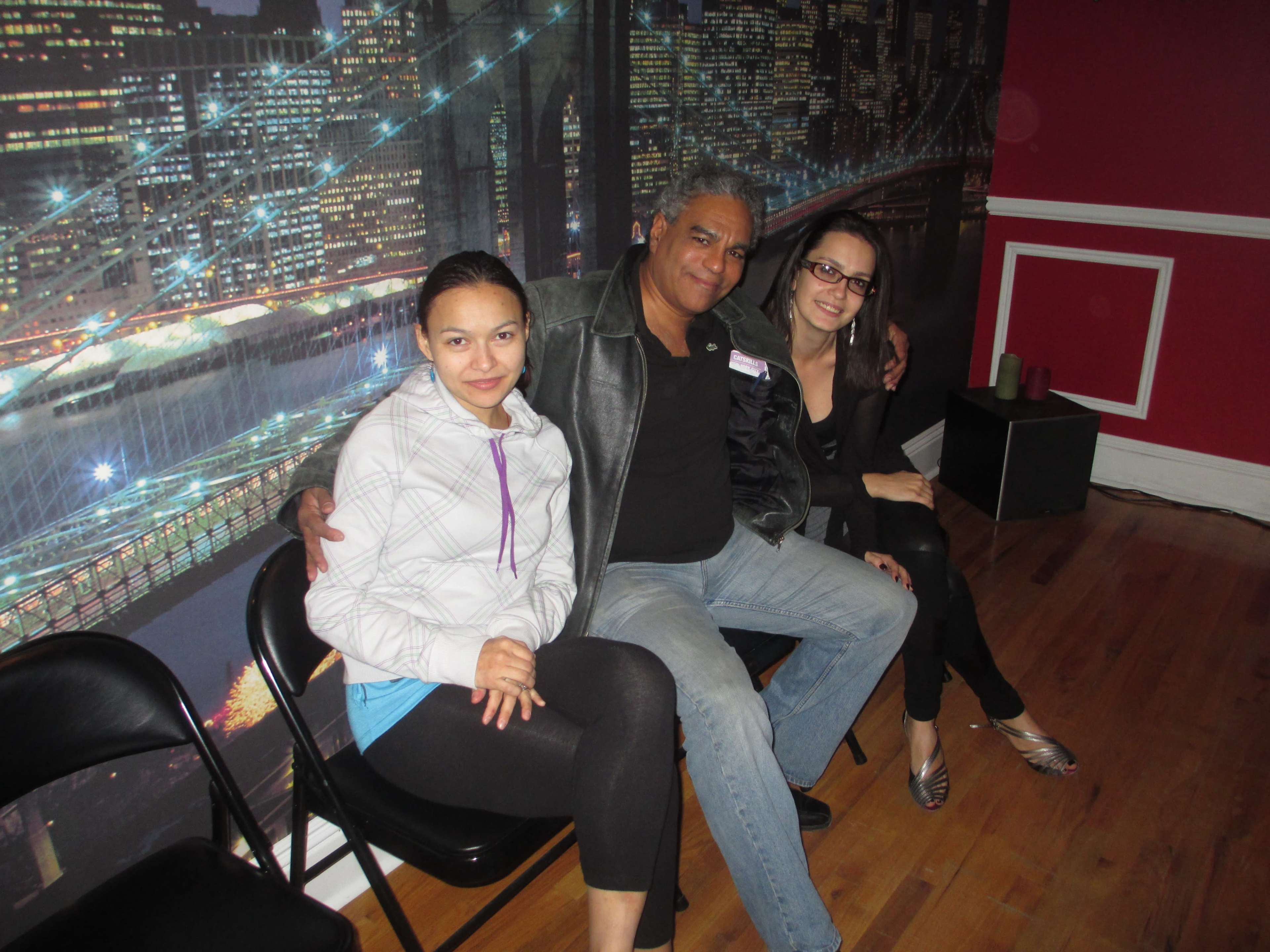 Three people are sitting on black chairs in front of a city skyline backdrop.