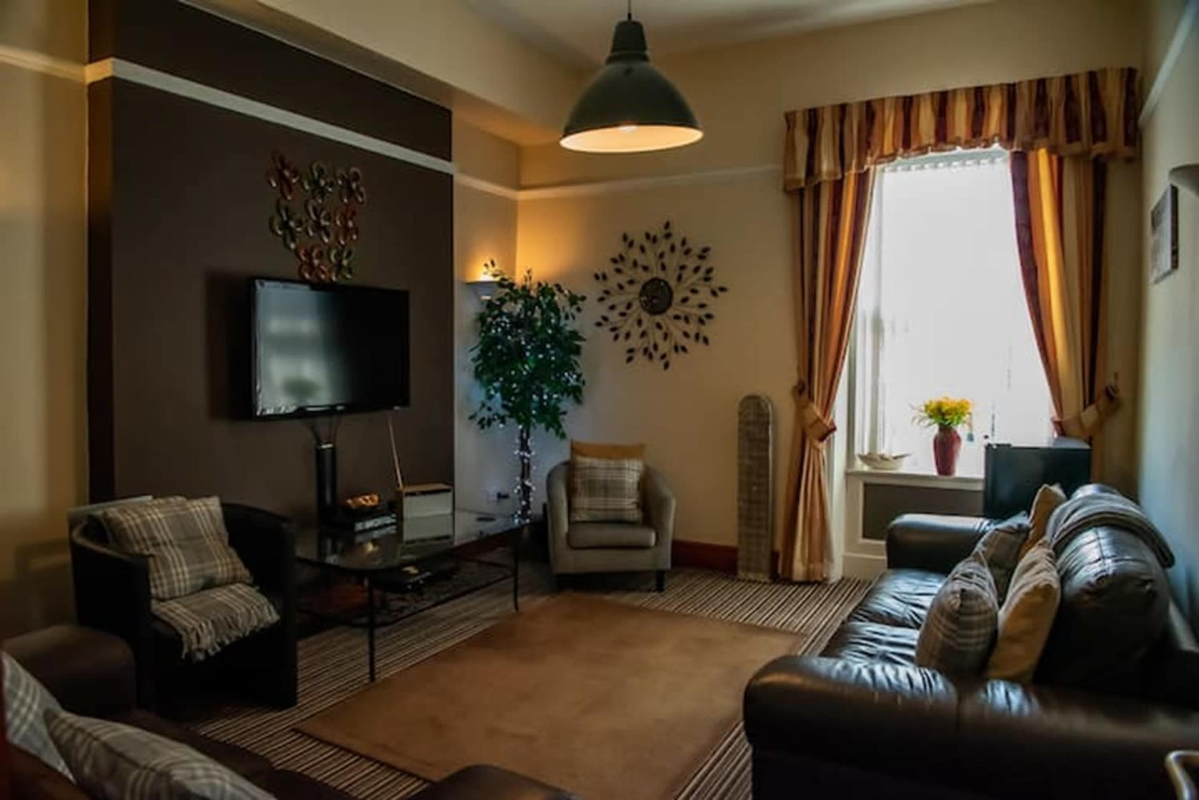 The image shows a cozy living room with dark walls, a large window draped in striped curtains, and a mix of comfortable seating including leather sofas and an armchair.