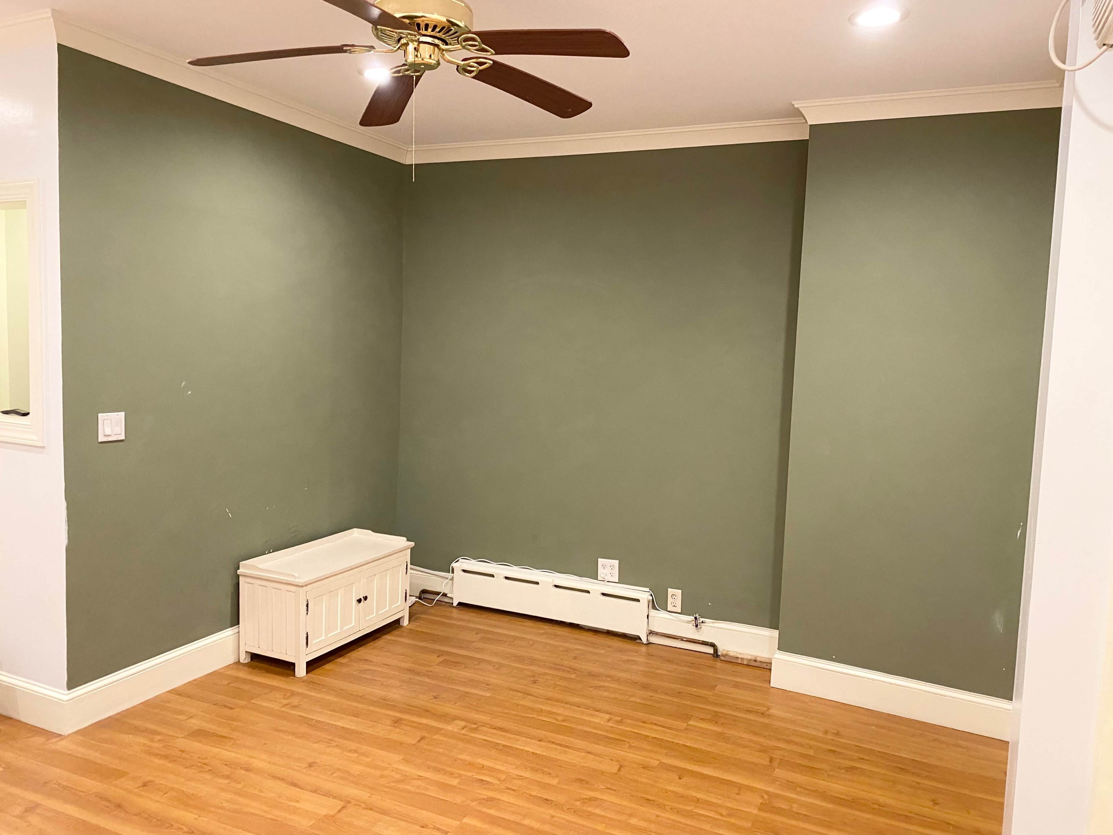 The image shows a room with a green accent wall, a wooden floor, a white cabinet, and a ceiling fan.