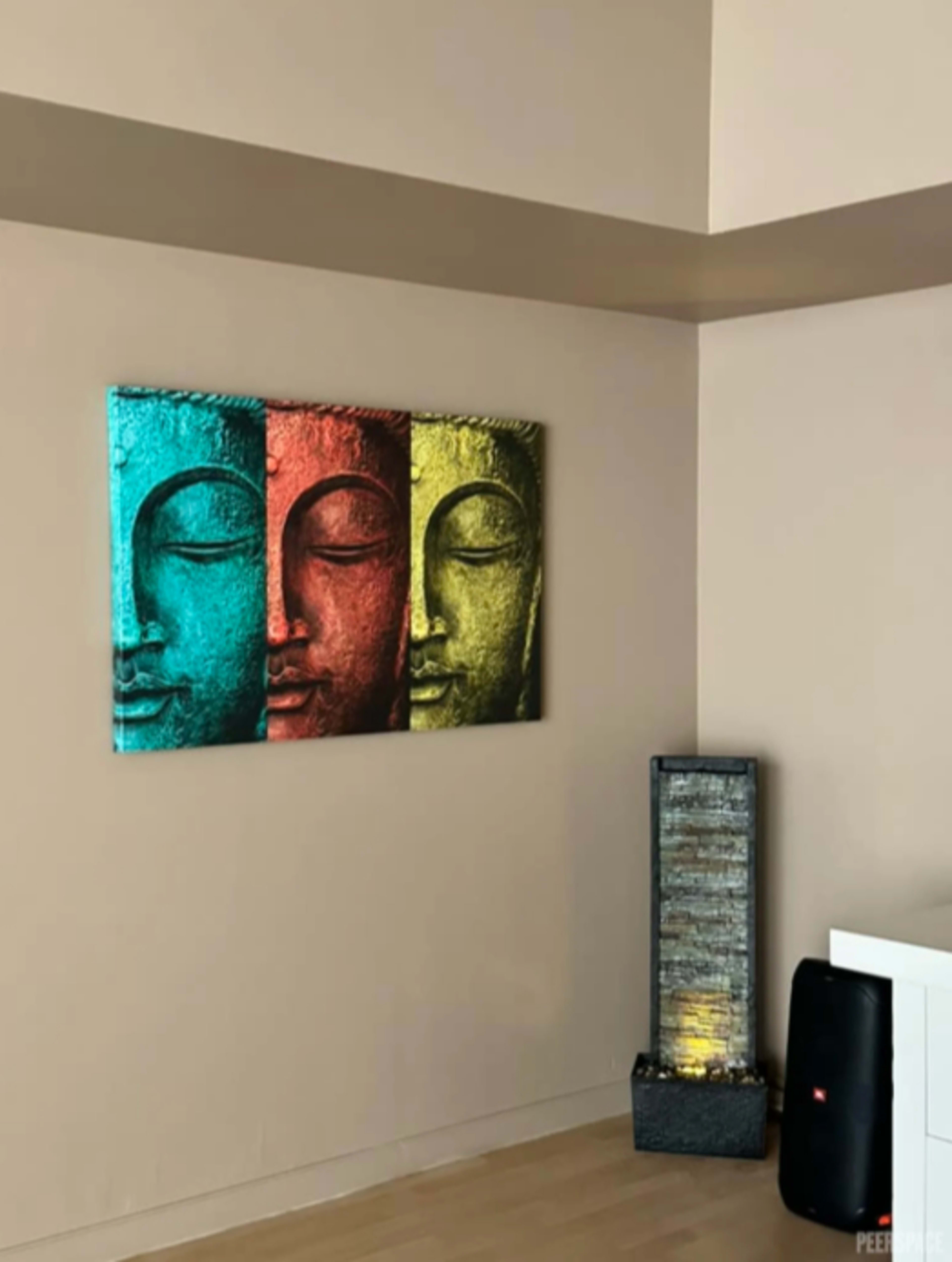 The image features a wall with a triptych of Buddha faces in blue, red, and yellow hues, along with a vertical water feature on the adjacent side.