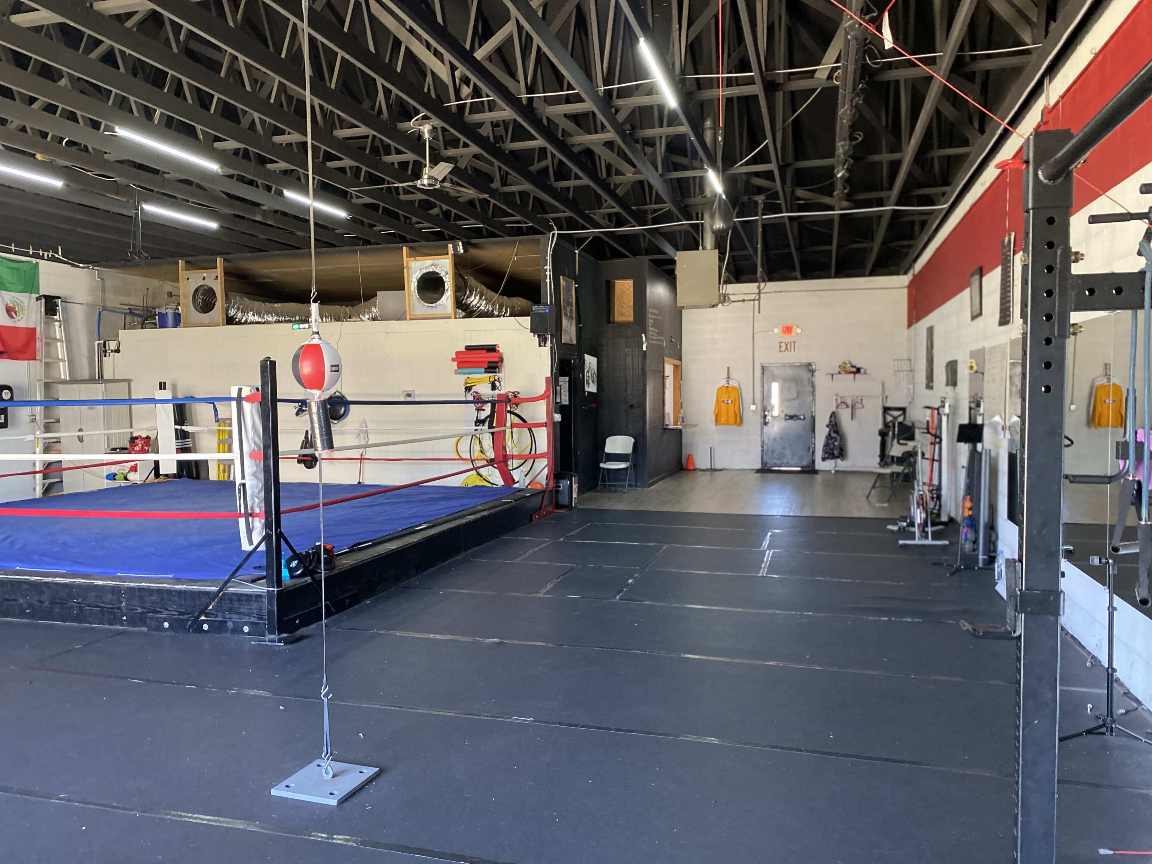 A boxing gym with a blue and red boxing ring, a variety of workout equipment, and a spacious training area.