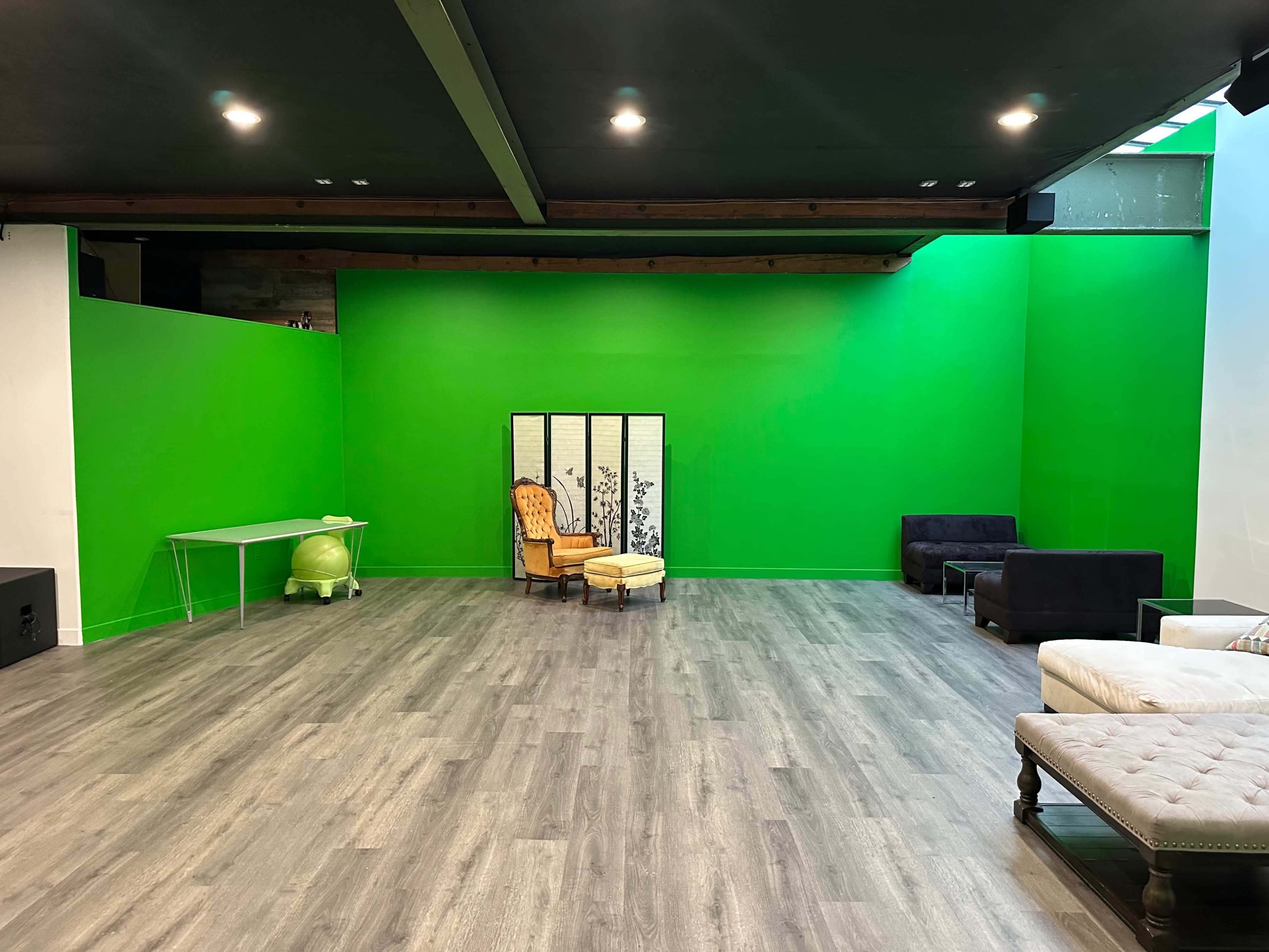 A spacious, sparsely furnished room with green walls, a wood floor, and various seating arrangements, including a folding screen and armchairs.
