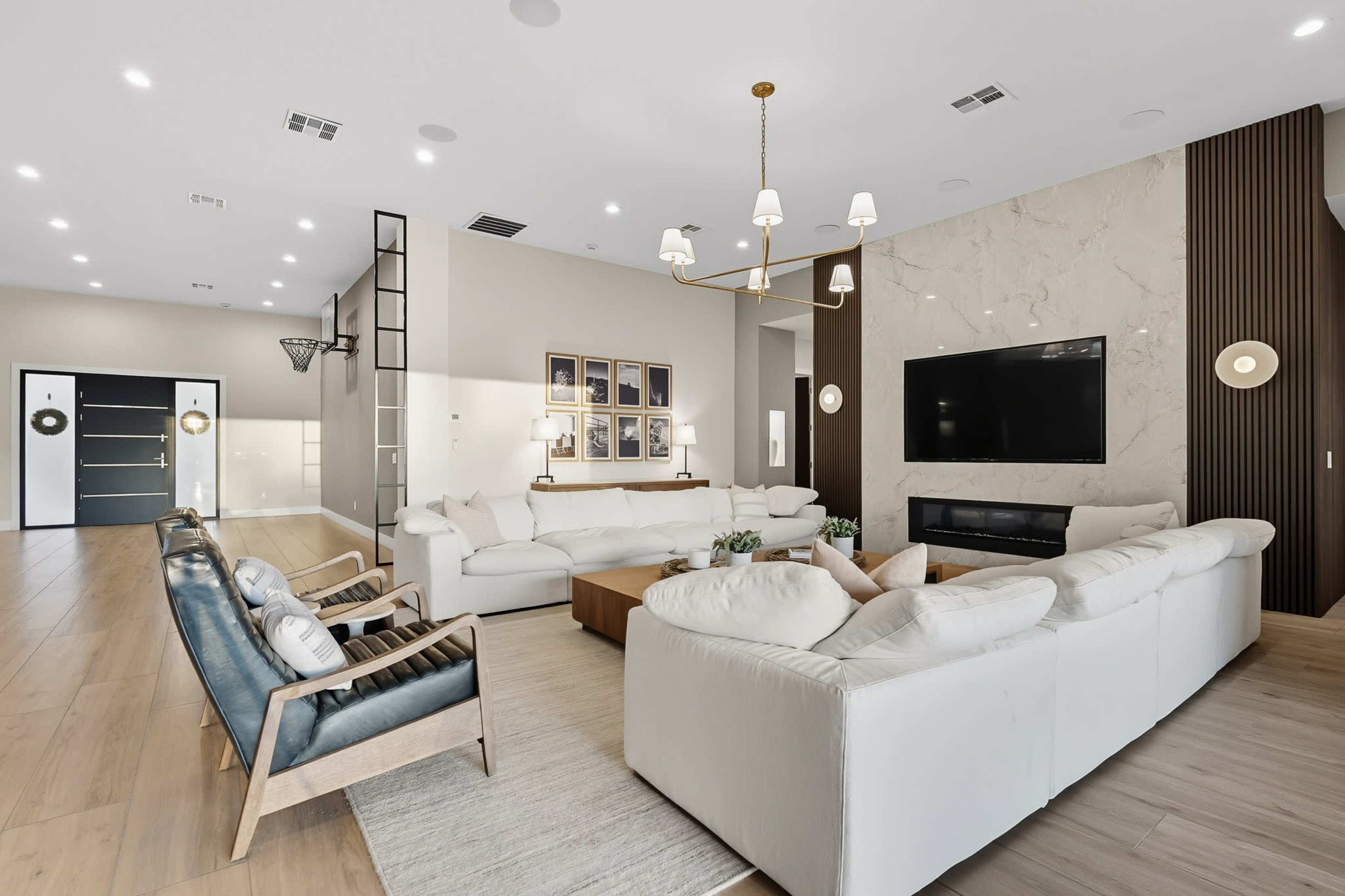 The image shows a modern living room with white sofas arranged around a coffee table, accented by a large television mounted on a marble wall.