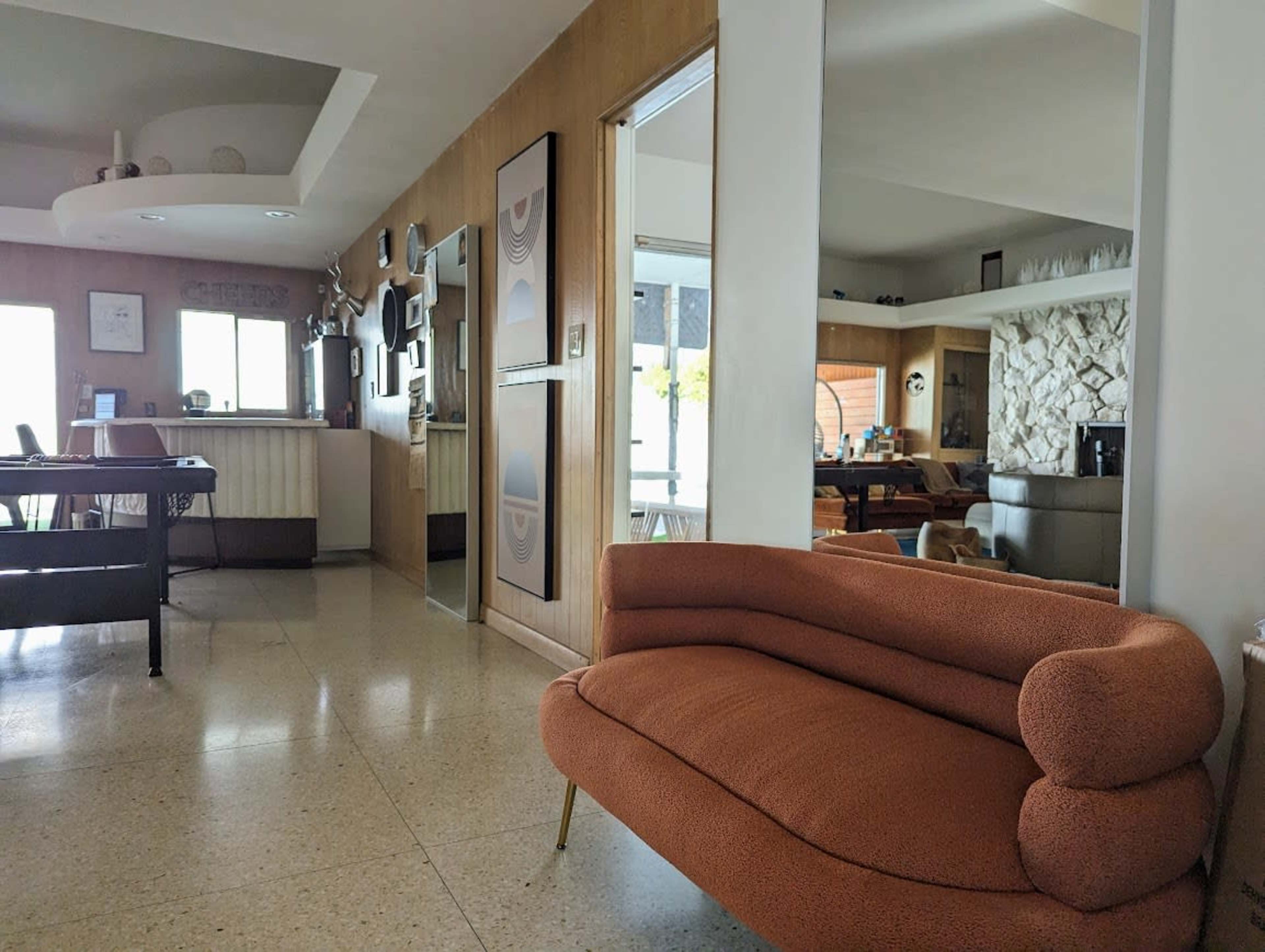 A modern living space with a curved orange couch, a dining area, and a kitchen partially visible in the background.