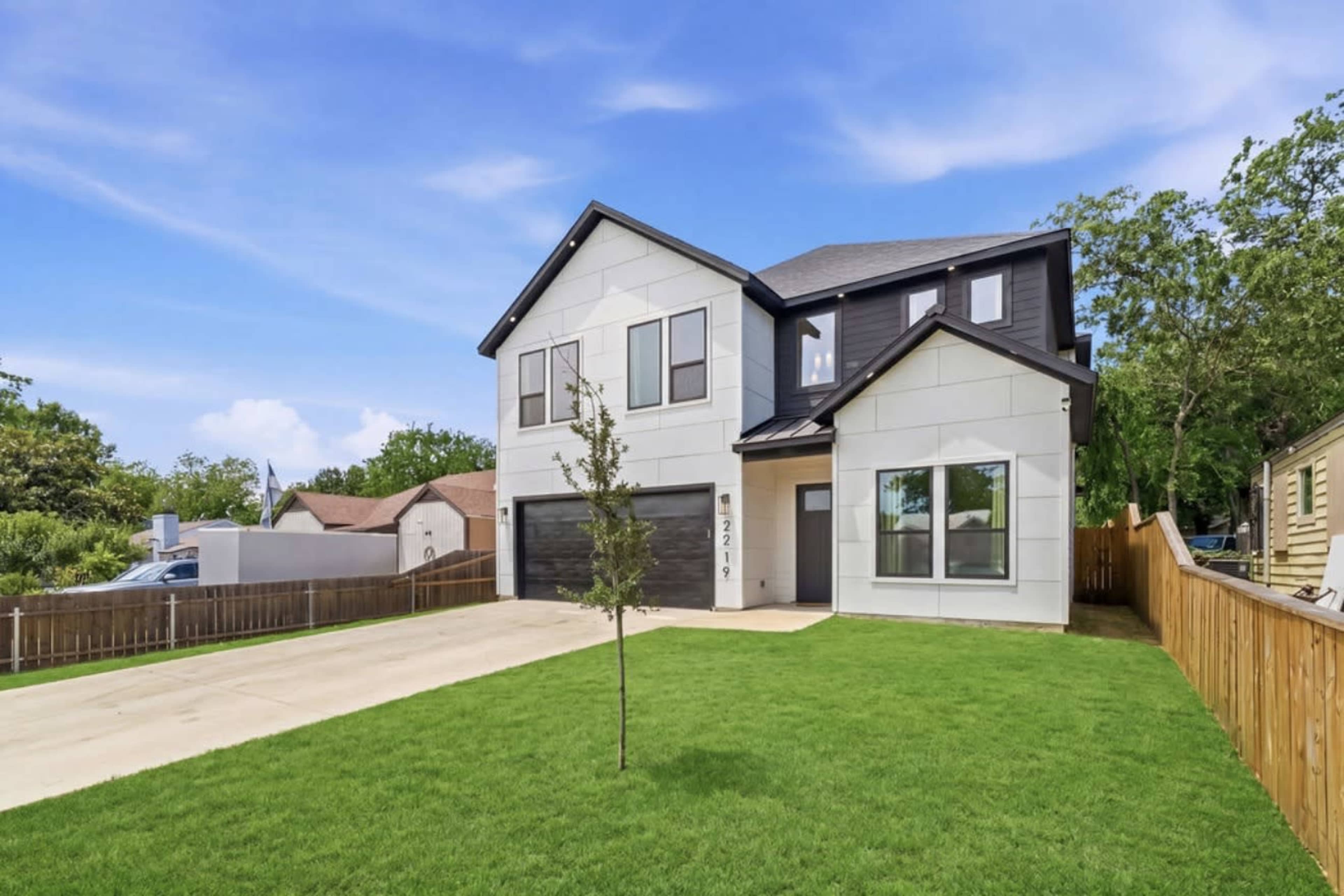 A modern two-story house with a black and white exterior, situated on a grassy lot with a concrete driveway.