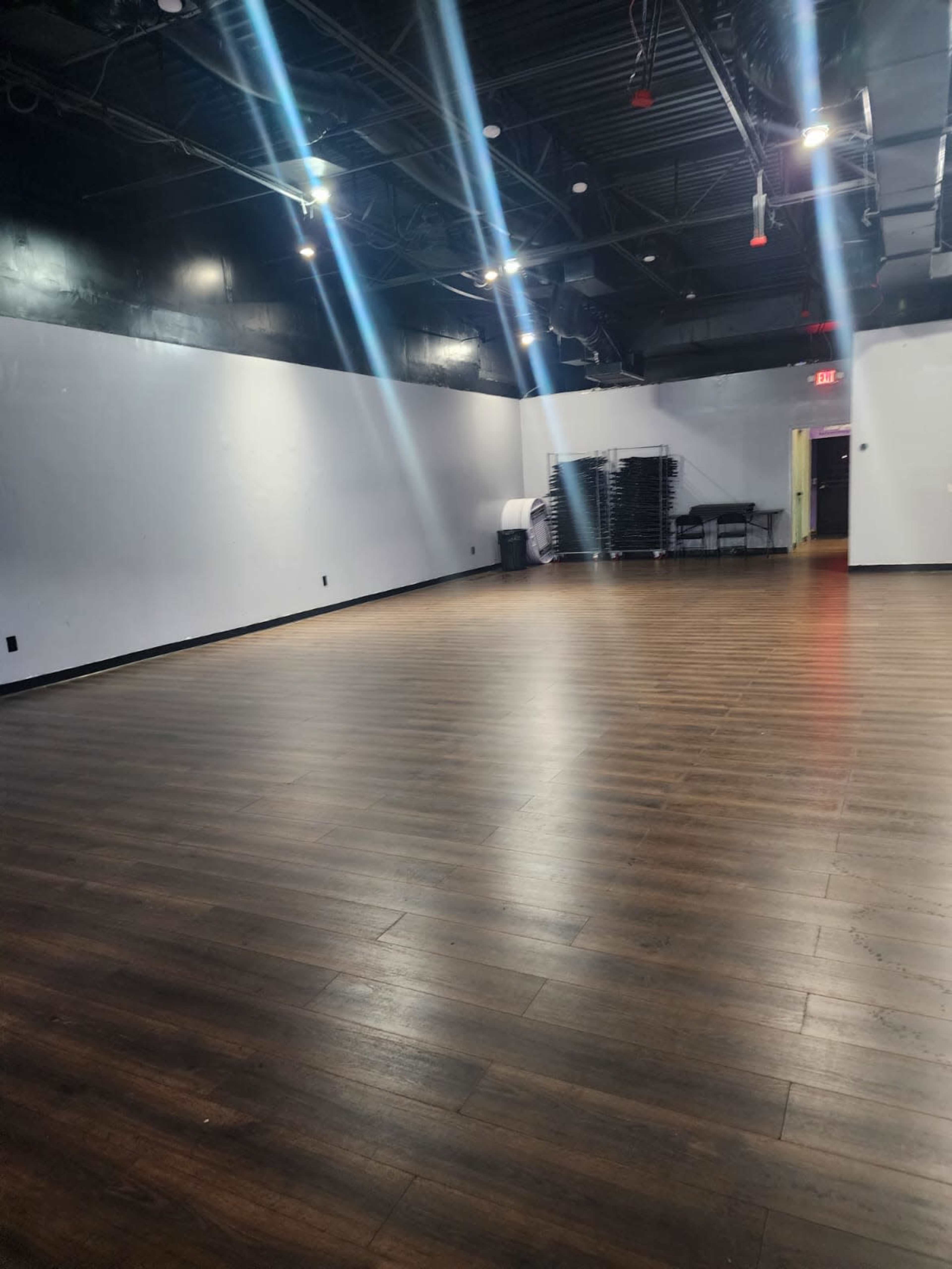The image shows an empty room with a wooden floor, black walls, and multiple overhead lights illuminating the space.