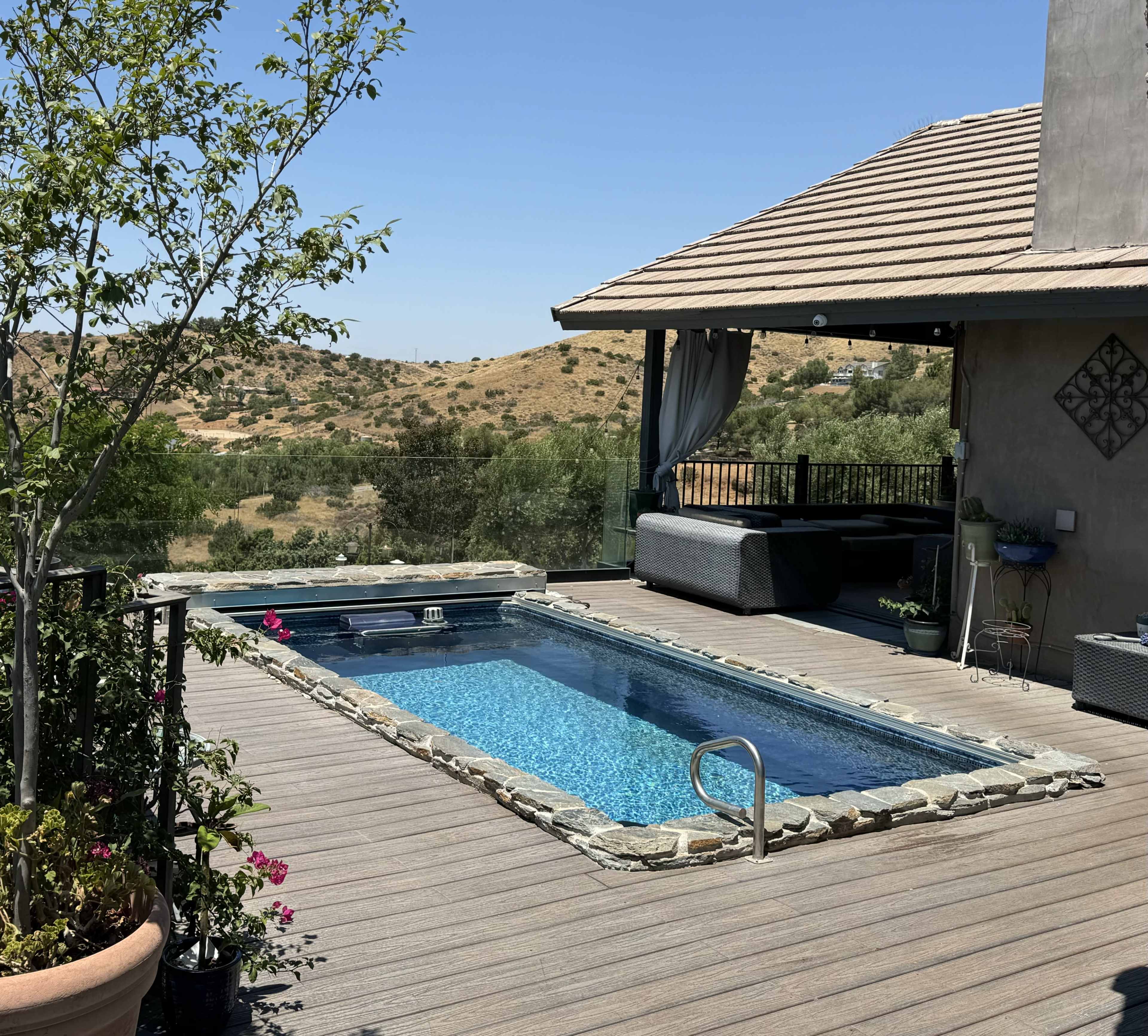 The image shows a small swimming pool surrounded by a wooden deck and overlooking a hilly landscape.