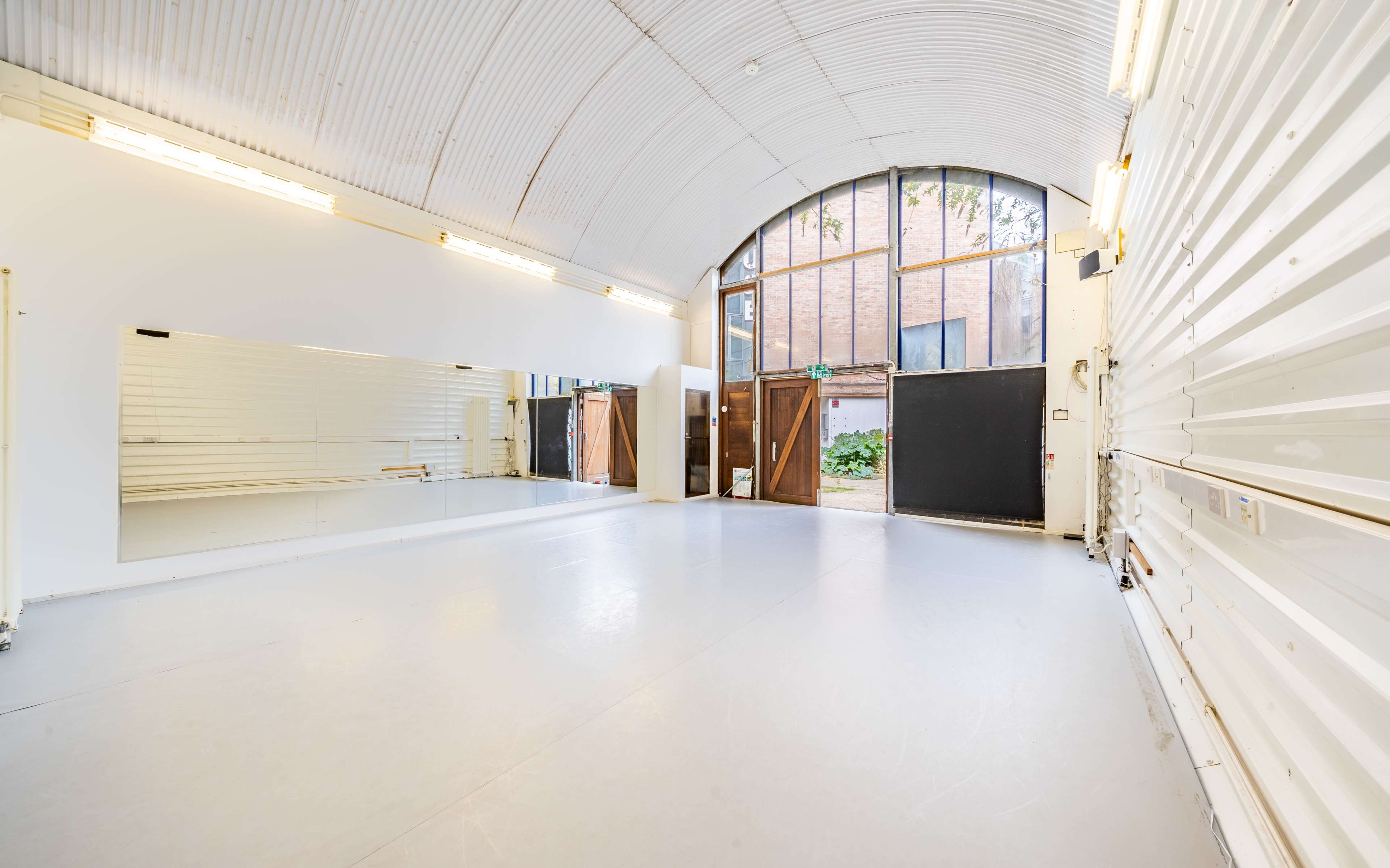 A spacious dance studio with a large mirror on one wall and double doors leading to an outdoor area.