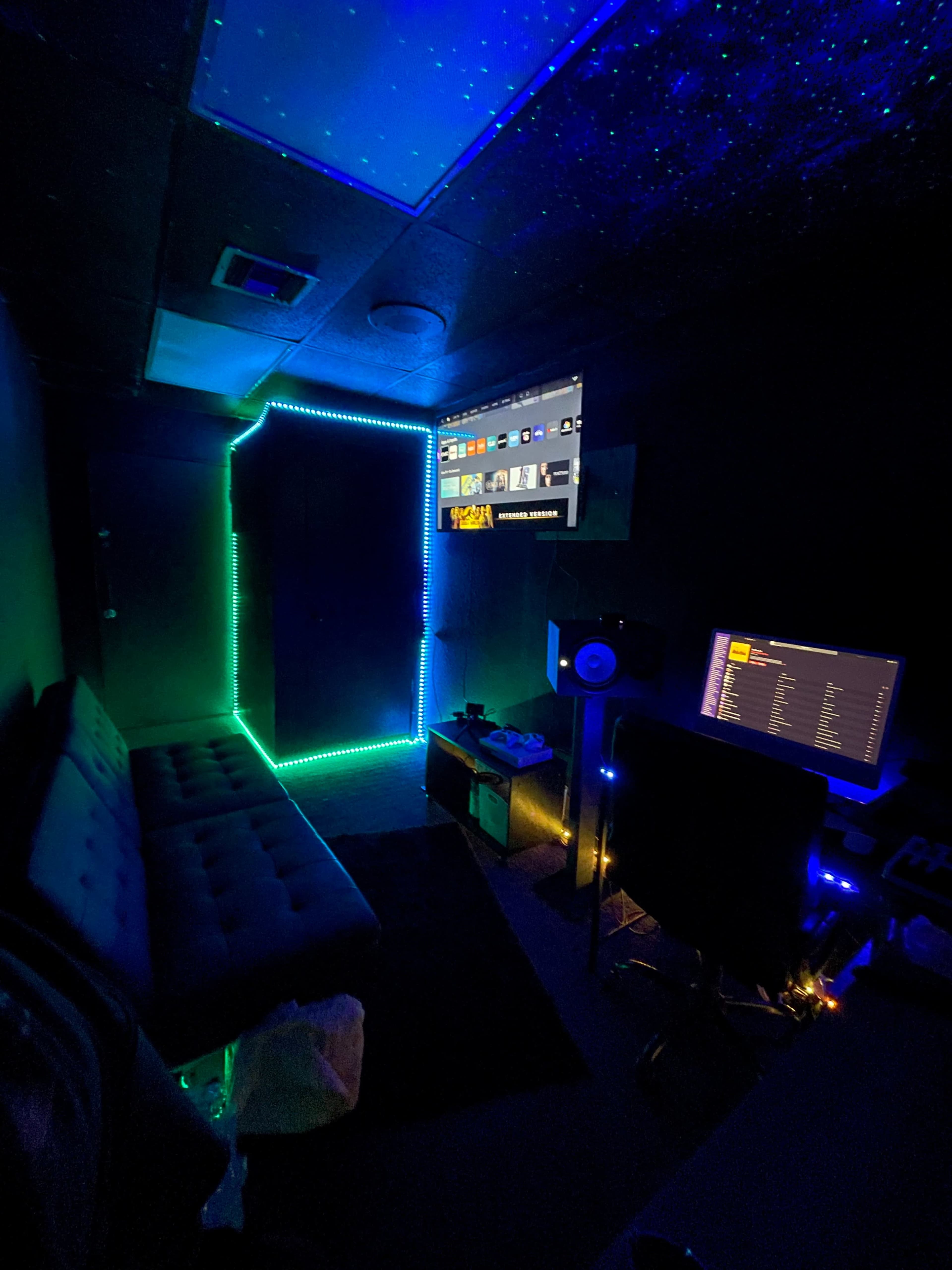 The image features a dimly lit room with neon LED lights outlining a door and surrounding a couch, along with a computer setup and a wall-mounted screen.